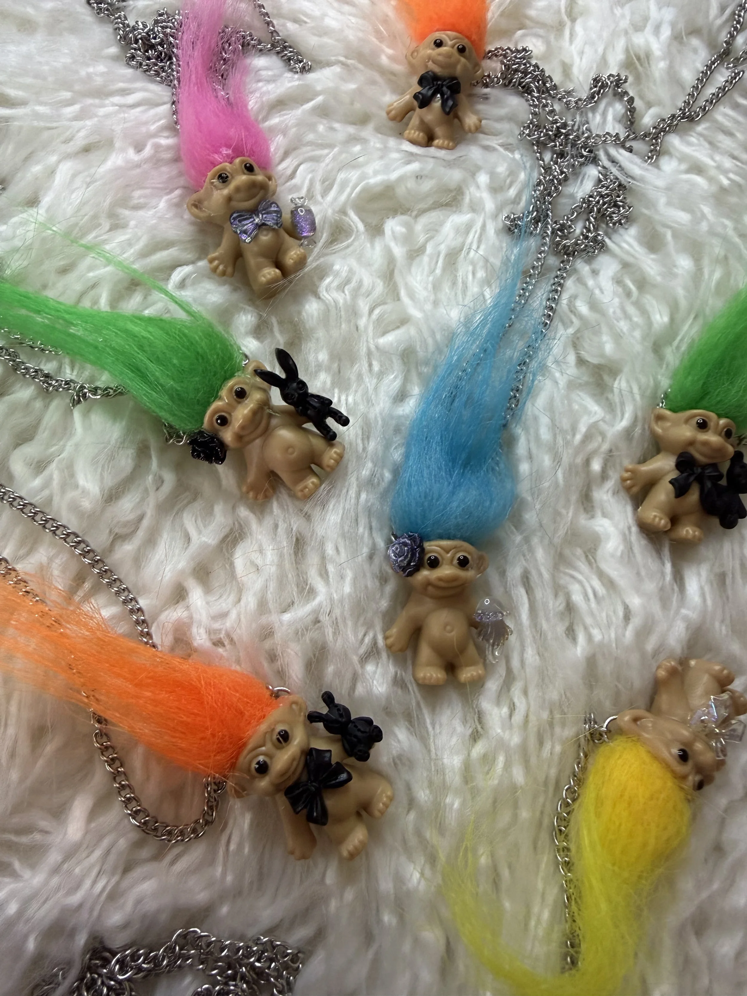 Colorful troll doll necklaces with bright hair and small black bunny charms on a white furry surface.