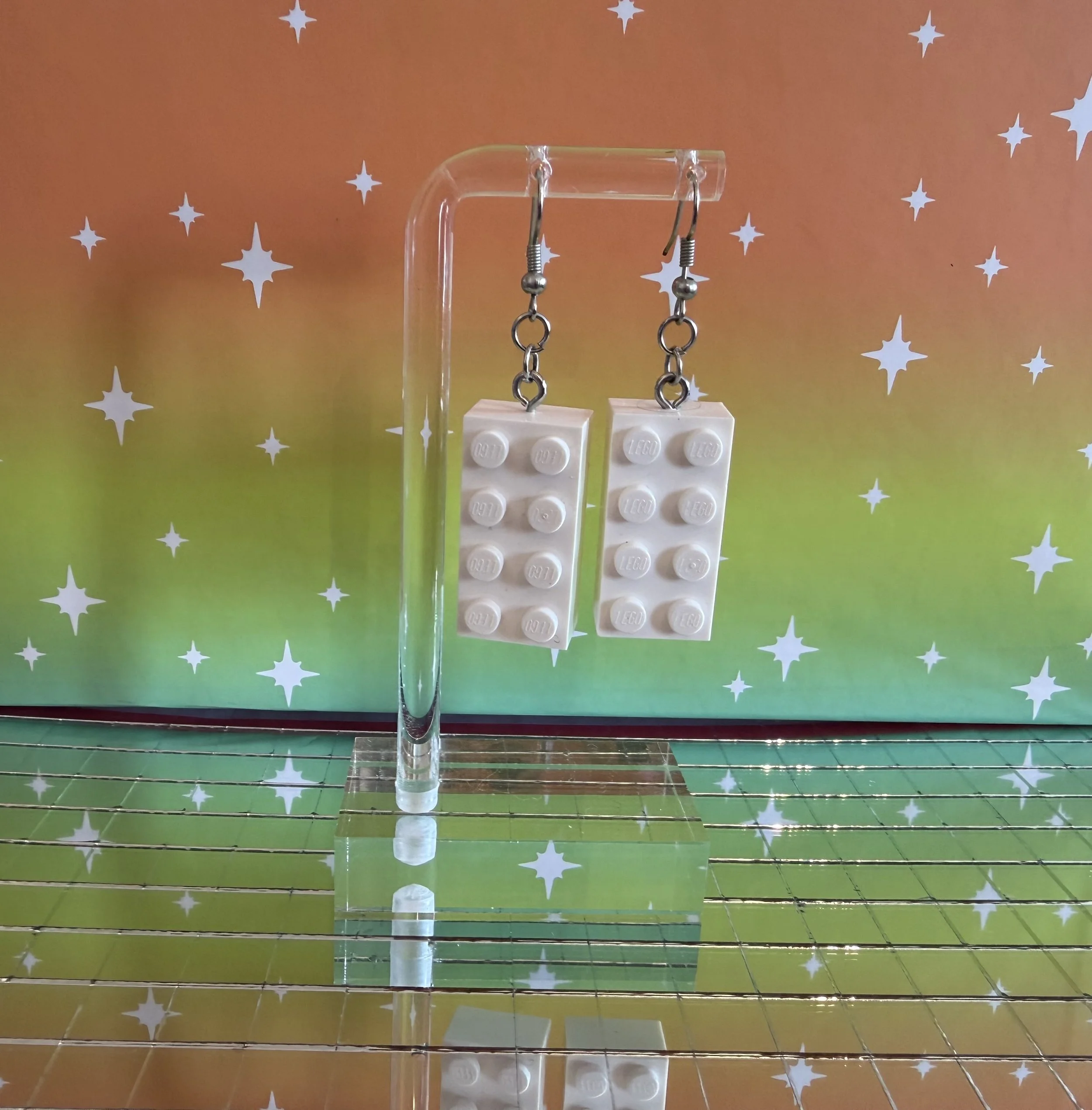 Earring display with two pairs of silver earrings hanging from a clear acrylic stand, background with a colorful galaxy pattern and white star shapes.