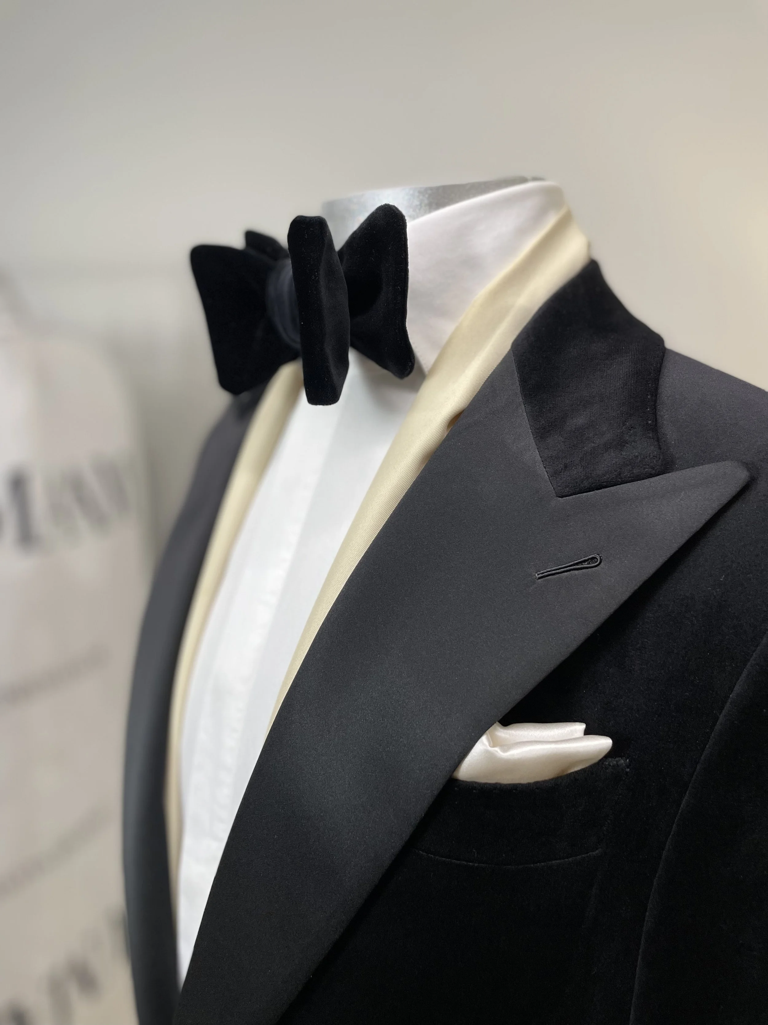 Close-up of a black tuxedo jacket and a white dress shirt with a black bow tie, with a cream-colored pocket square in the breast pocket.