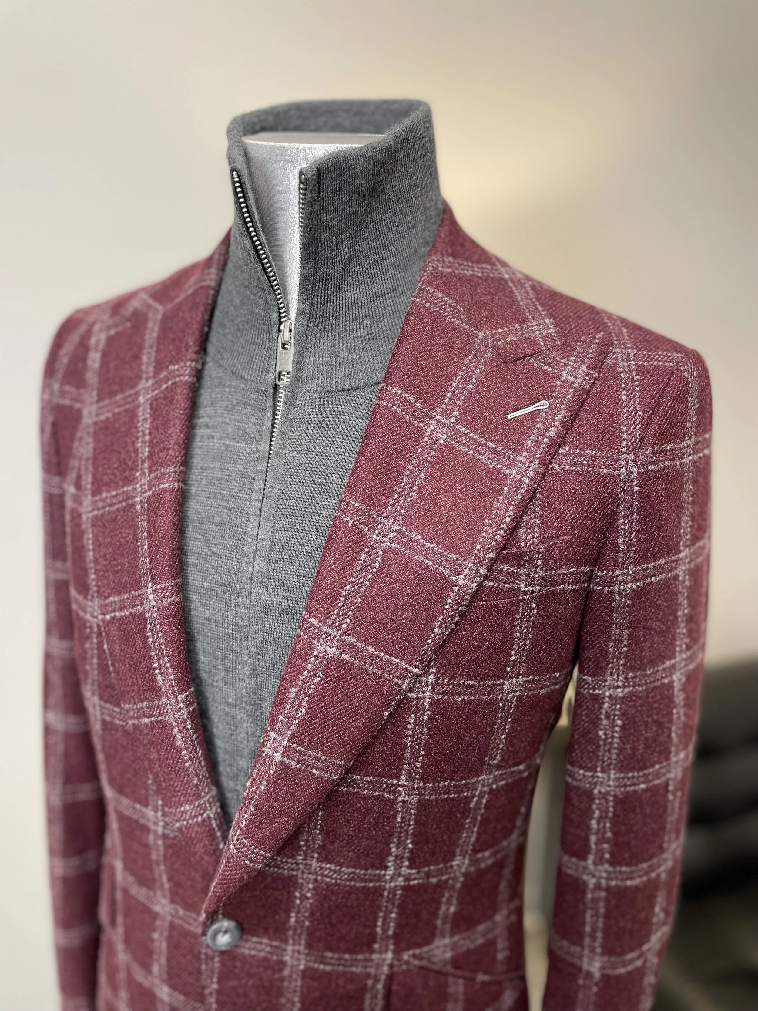 A mannequin dressed in a red plaid blazer with a gray zip-up mock turtleneck underneath.