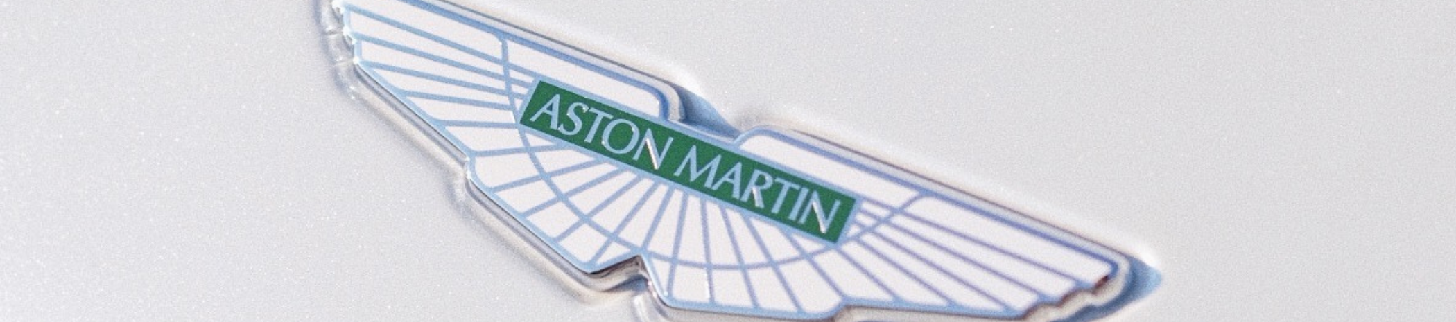 Close-up of an Aston Martin logo badge on a white car.
