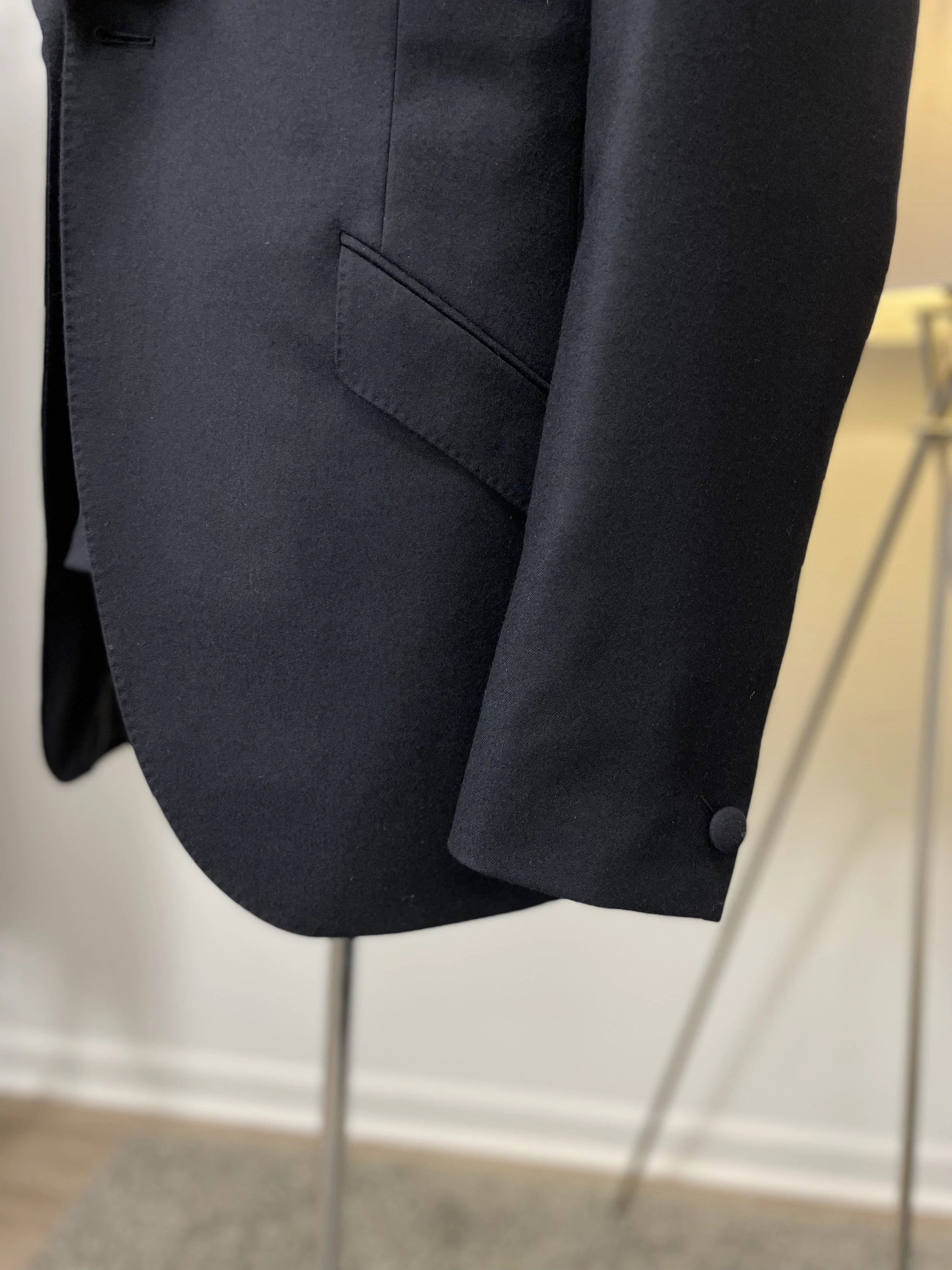 Close-up of the bottom corner of a black suit jacket, showing a pocket and the sleeve with a button.