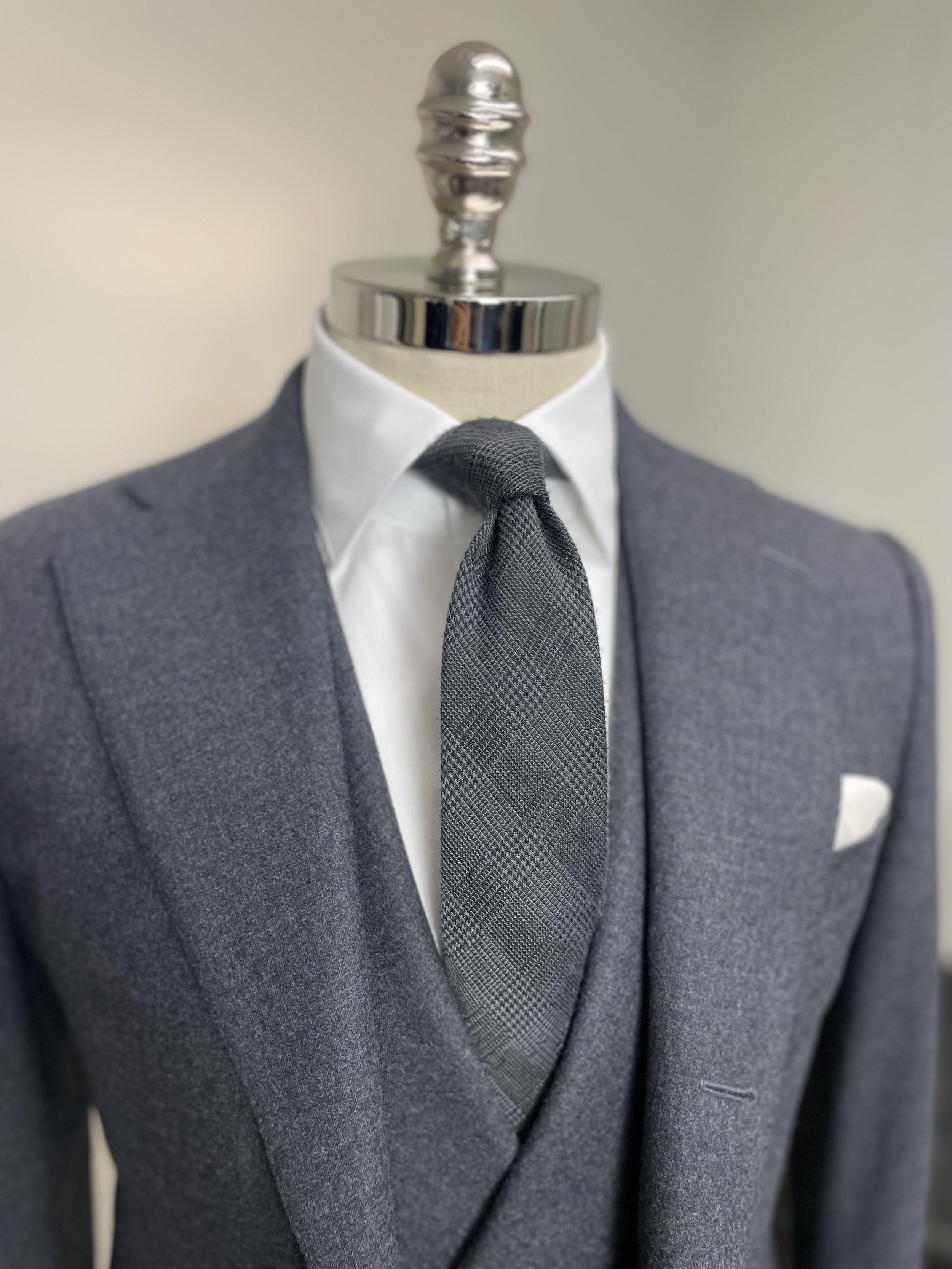 Men's mannequin dressed in a gray suit, white shirt, gray tie with a plaid pattern, and a white pocket square.