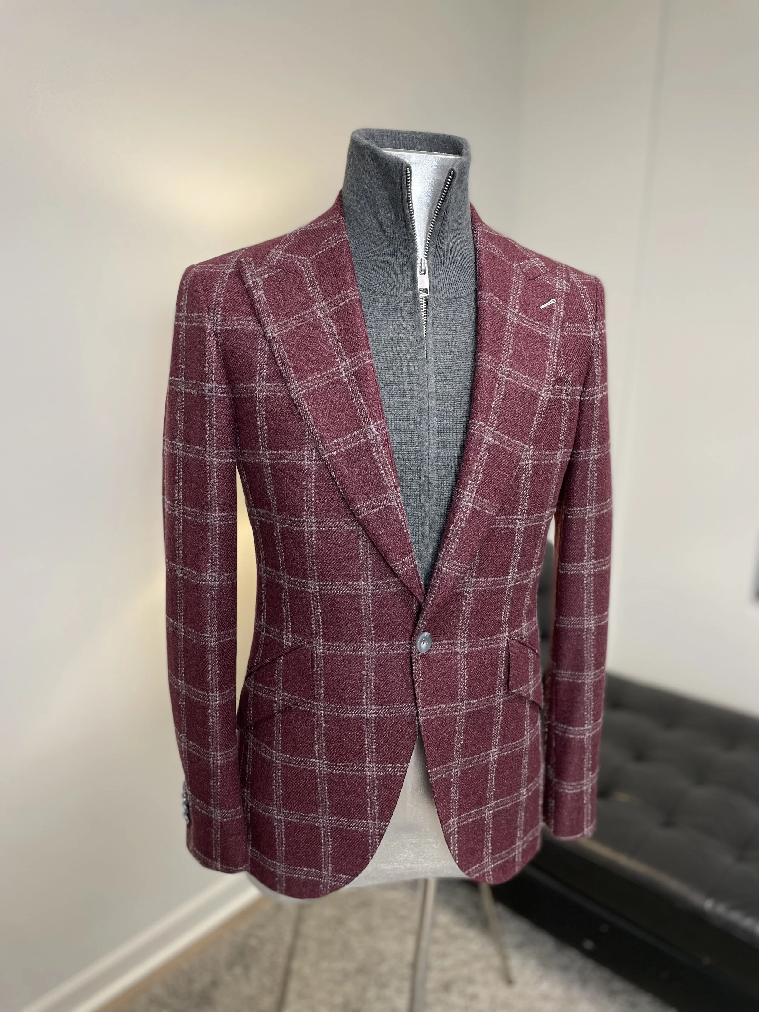 A mannequin wearing a maroon plaid blazer over a gray zip-up sweater.
