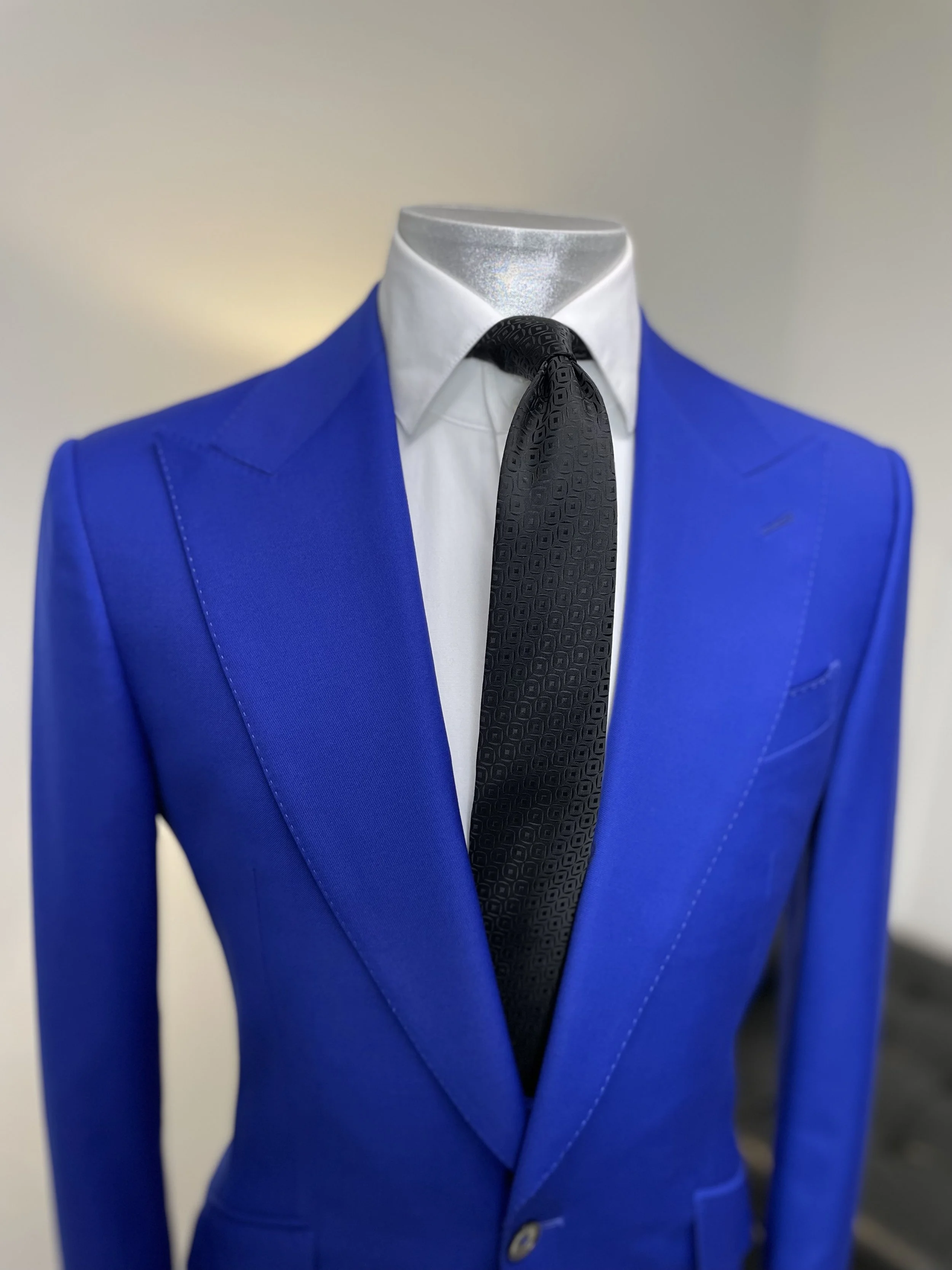 A mannequin dressed in a blue suit with a white shirt and a black patterned tie.