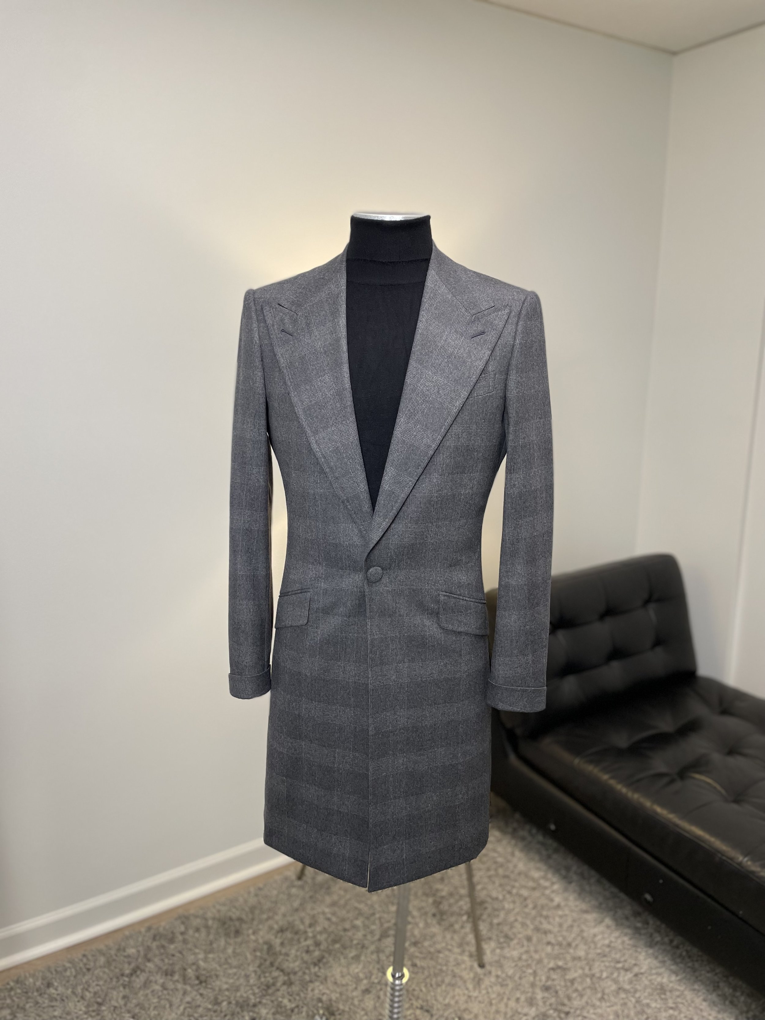 Gray plaid women's blazer coat displayed on a mannequin, with a black turtleneck underneath, in a room with a black sofa in the background.