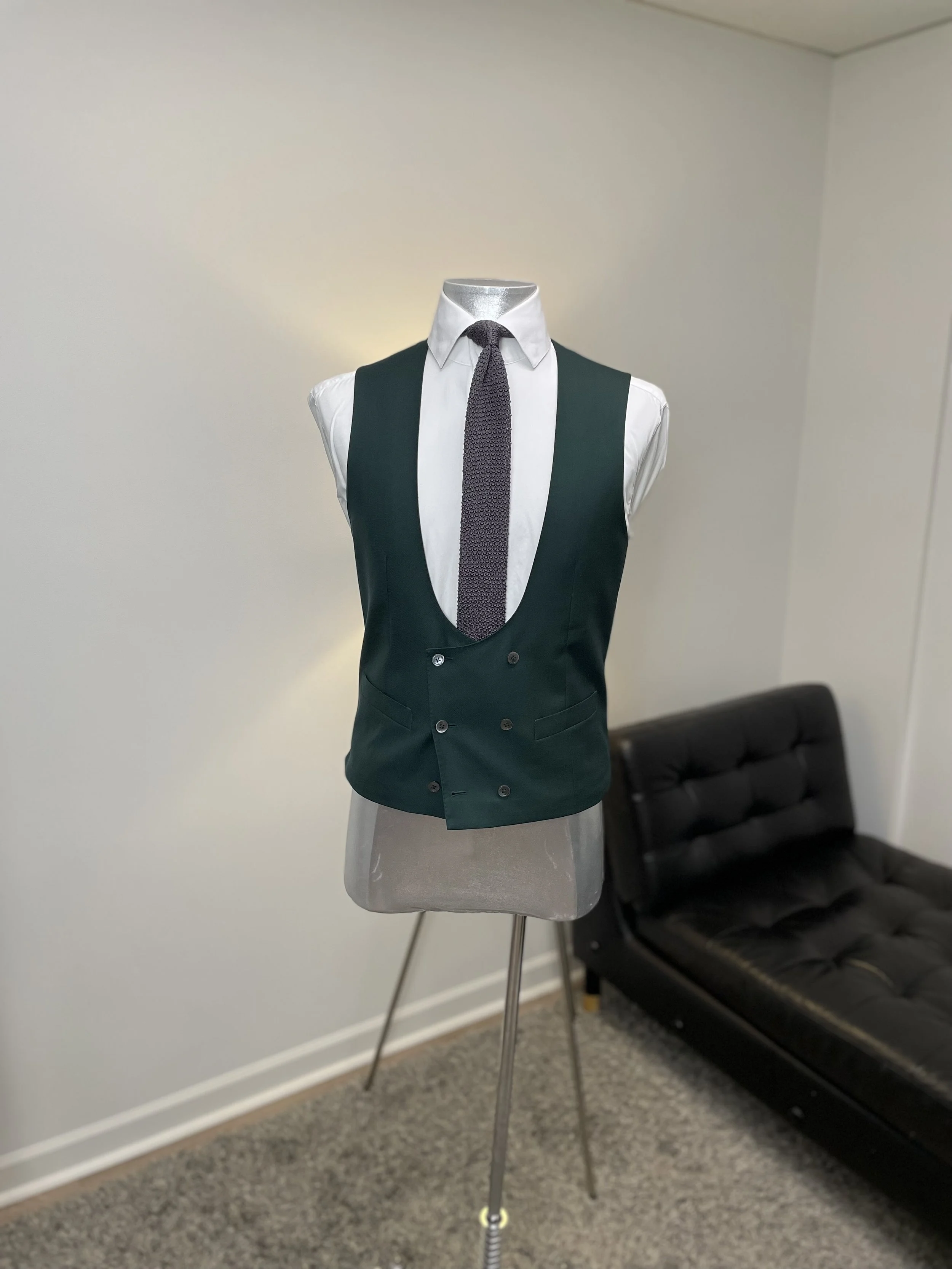 Tailored men's vest over a white dress shirt with a dark tie on a mannequin, in an office setting.