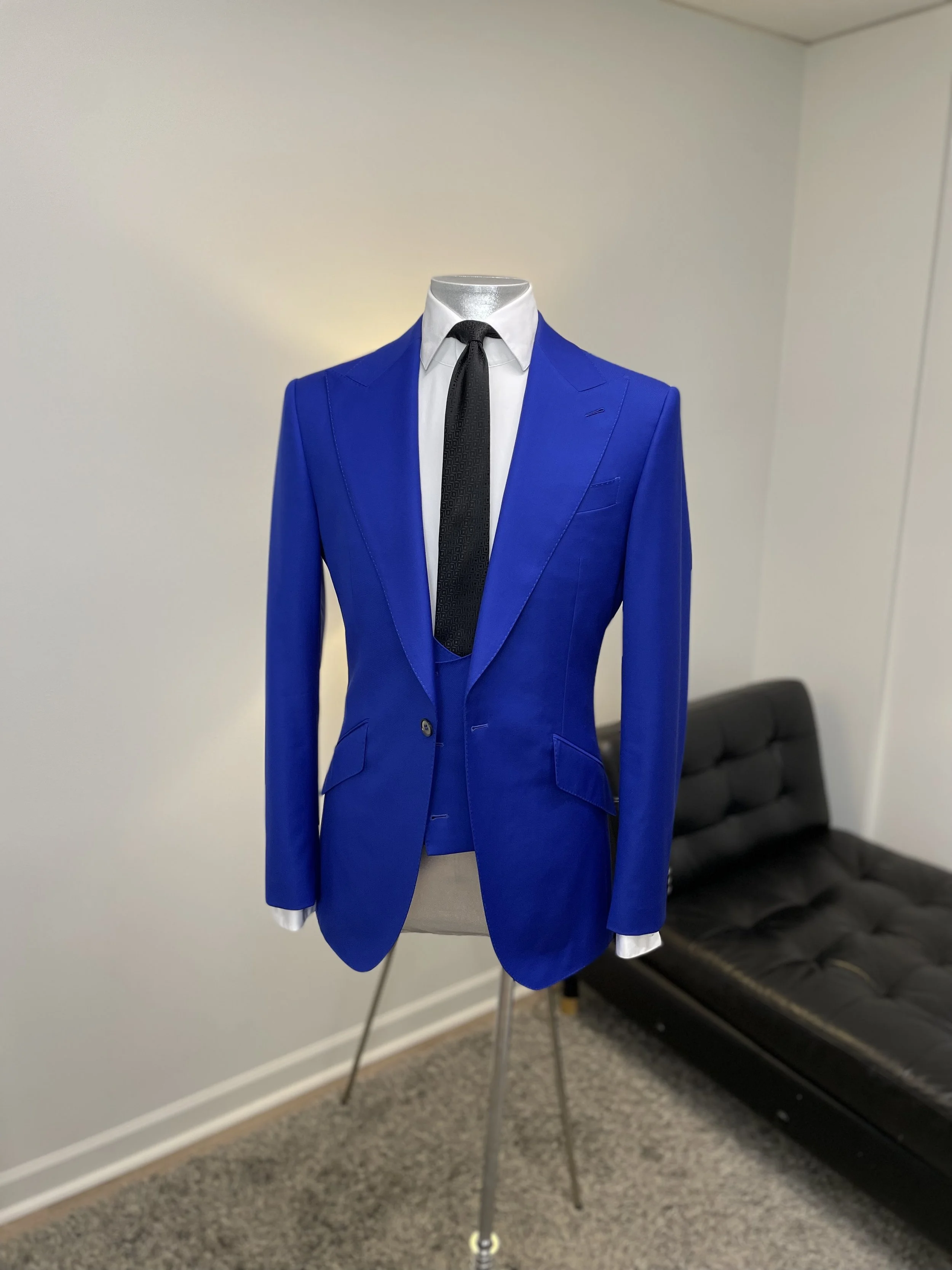 Blue suit jacket on a mannequin, paired with a white shirt and black tie, standing next to a black futon.