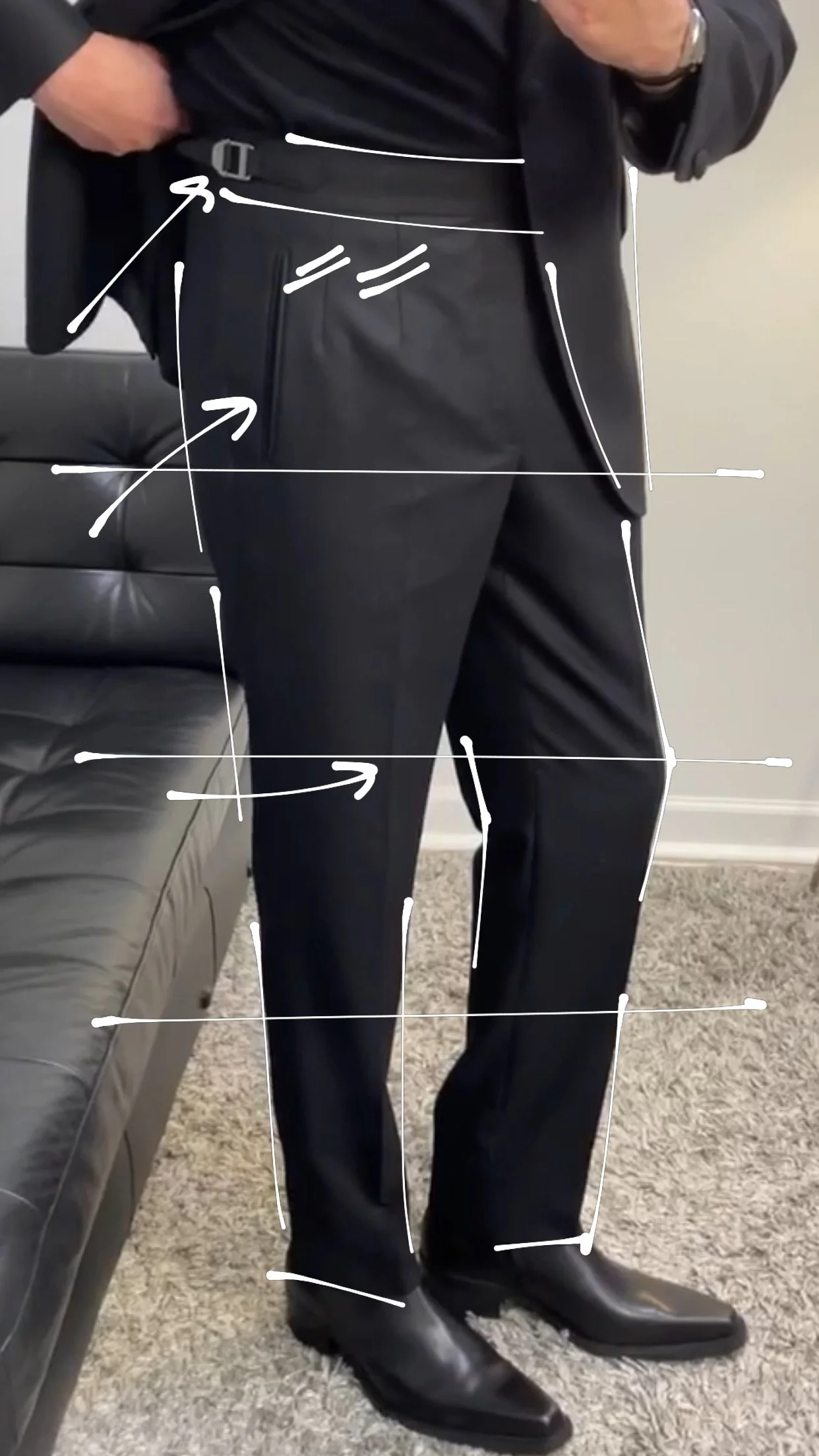 Person wearing black dress pants and a dark jacket, standing with one hand in pocket, with white lines and arrows pointing out different parts of the outfit.