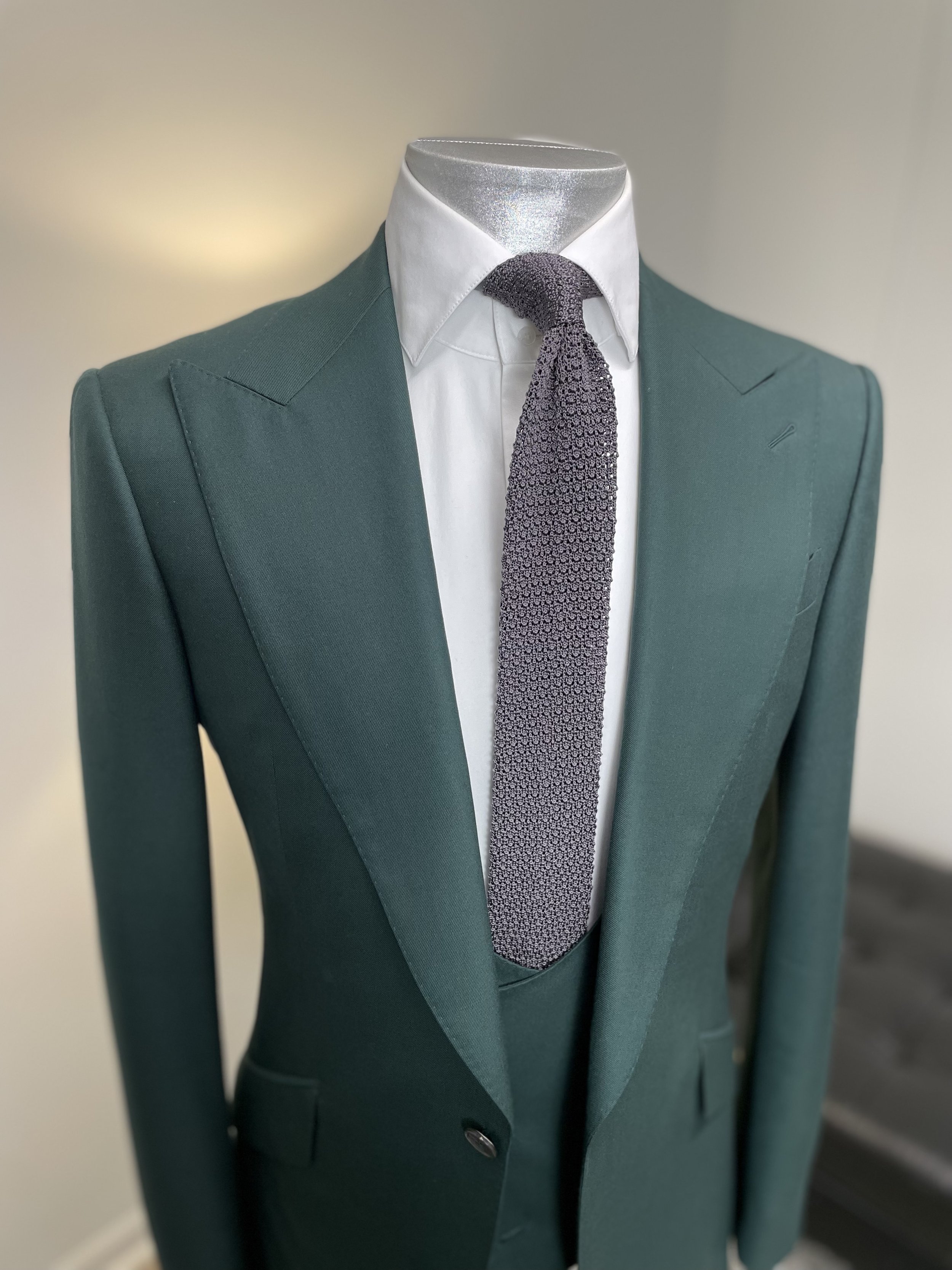 Green suit with a white dress shirt and a textured dark tie on a mannequin.