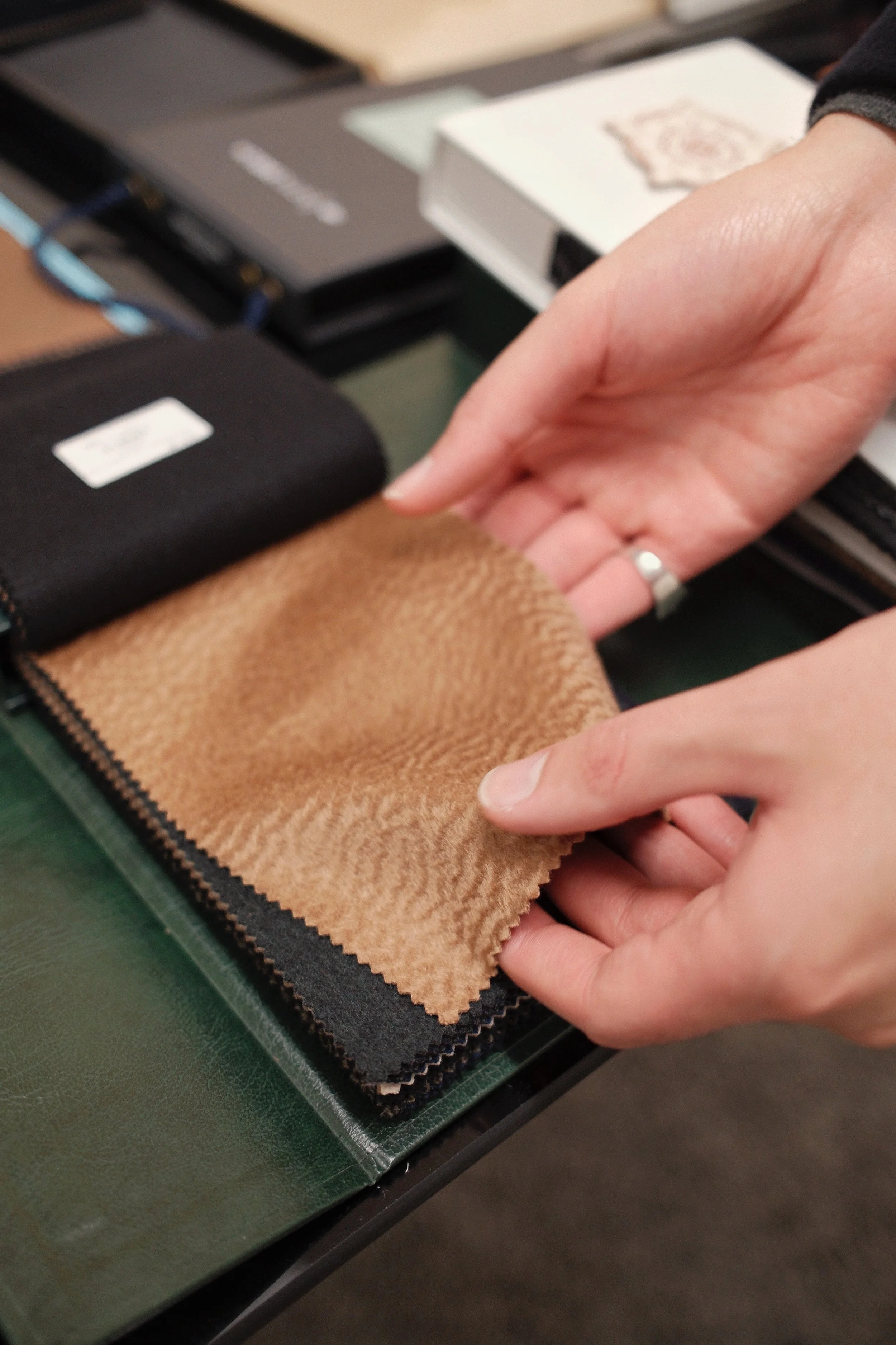 Person holding a brown fabric sample swatch over other fabric samples on a table.