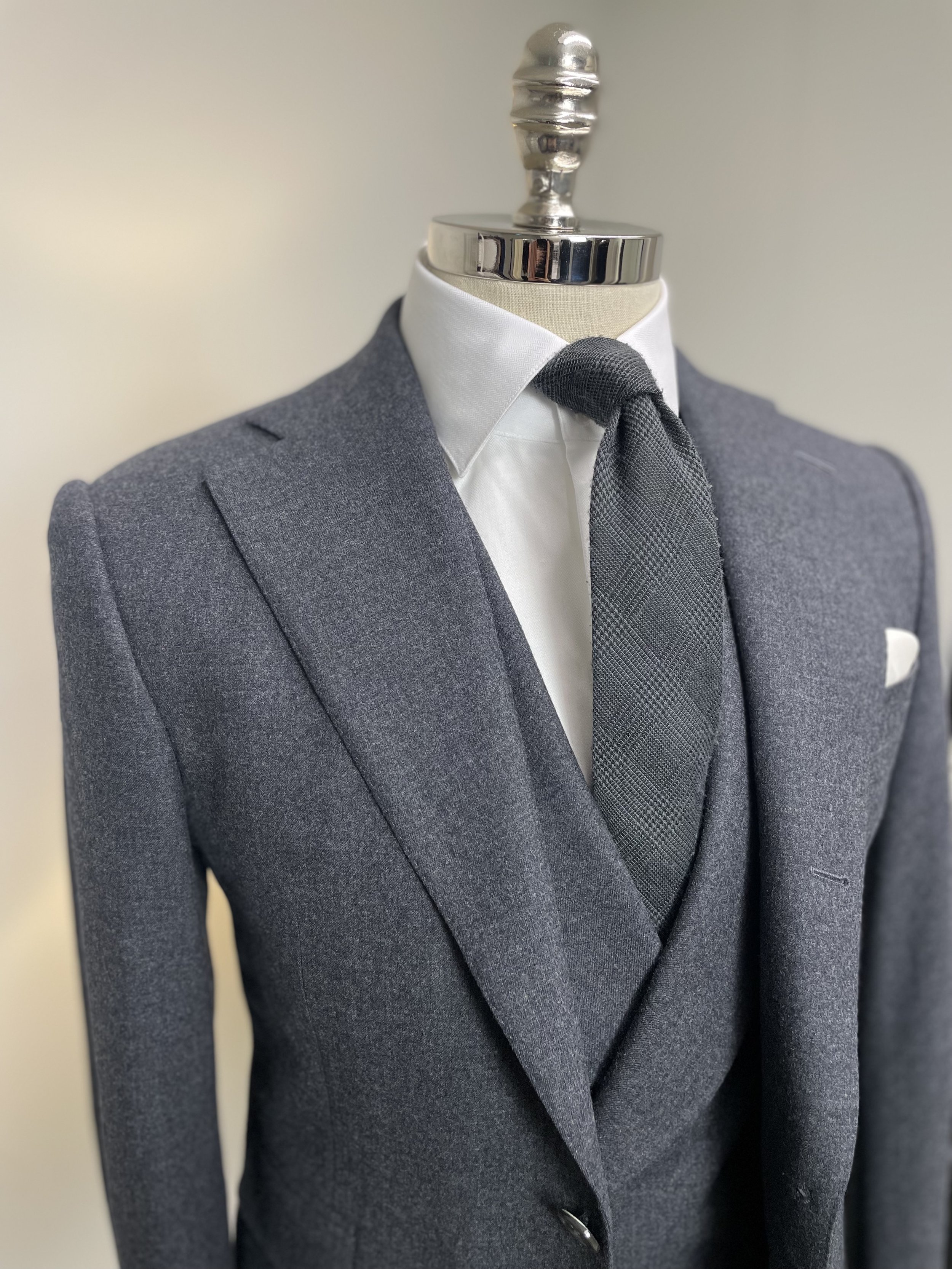 Grey suit on a mannequin with white shirt, dark patterned tie, and white pocket square.