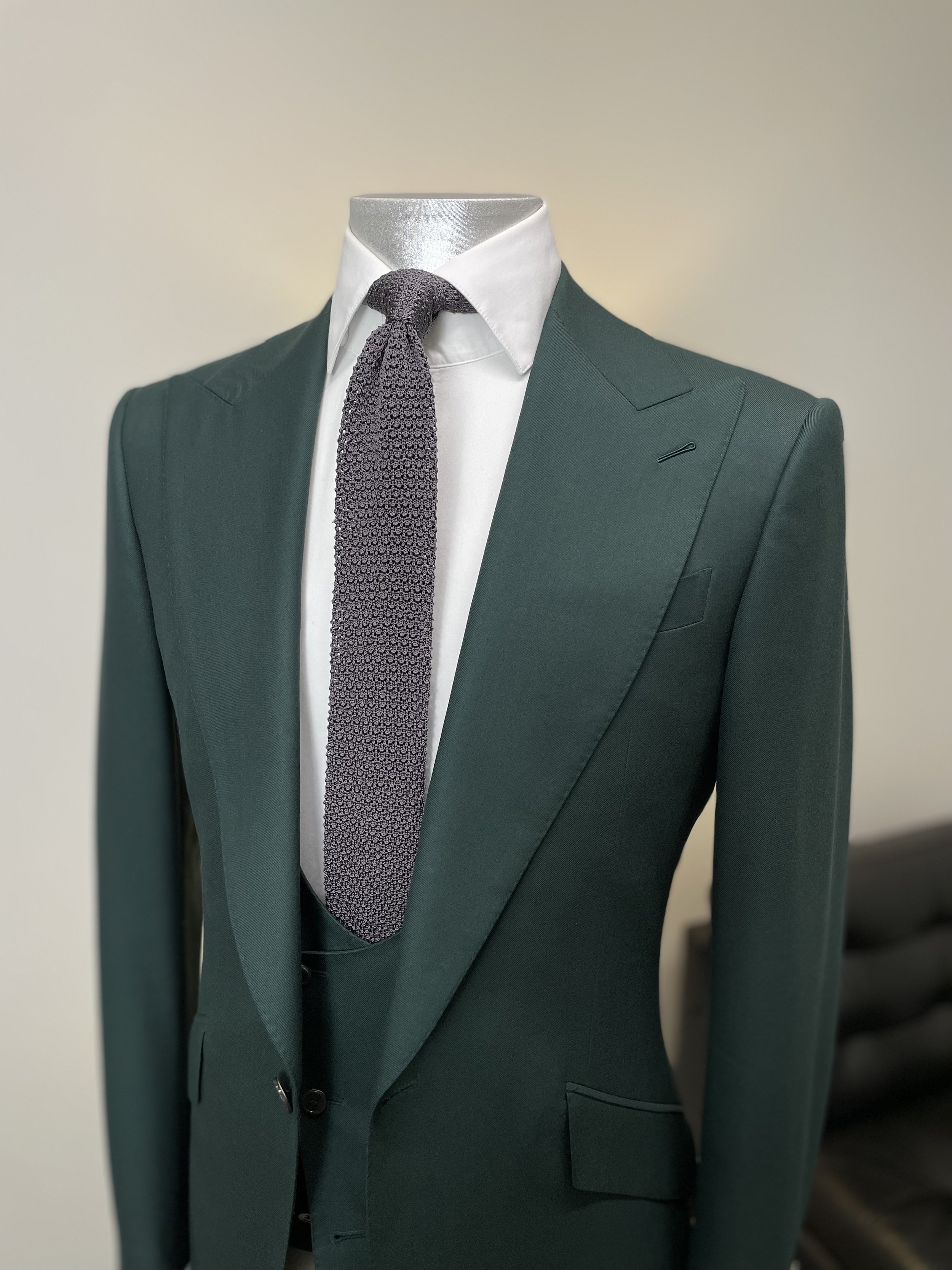 Green suit jacket with white dress shirt and gray textured tie on a mannequin, indoors.