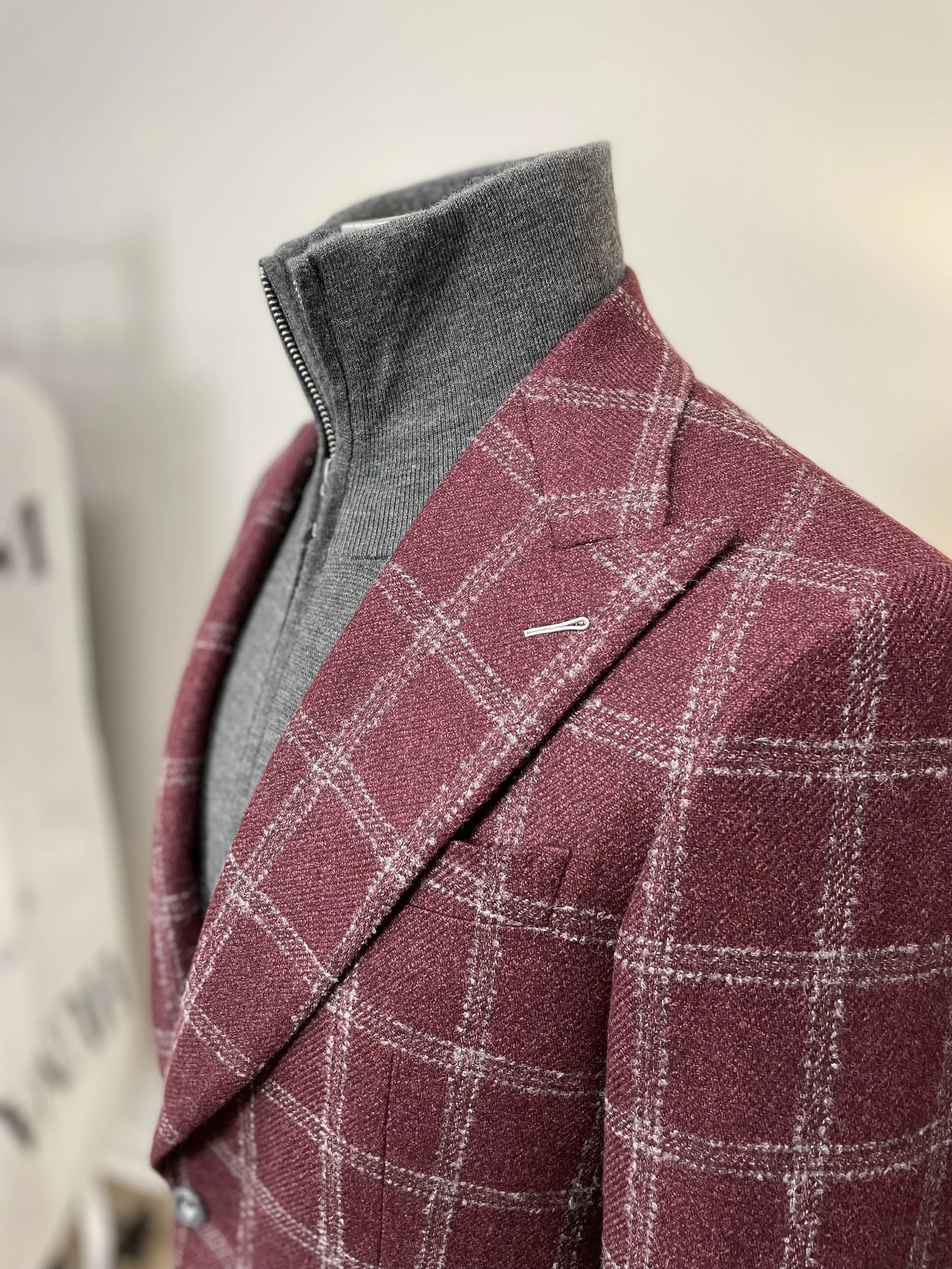 Close-up of a mannequin dressed in a red plaid blazer with a grey zip-up sweater underneath.