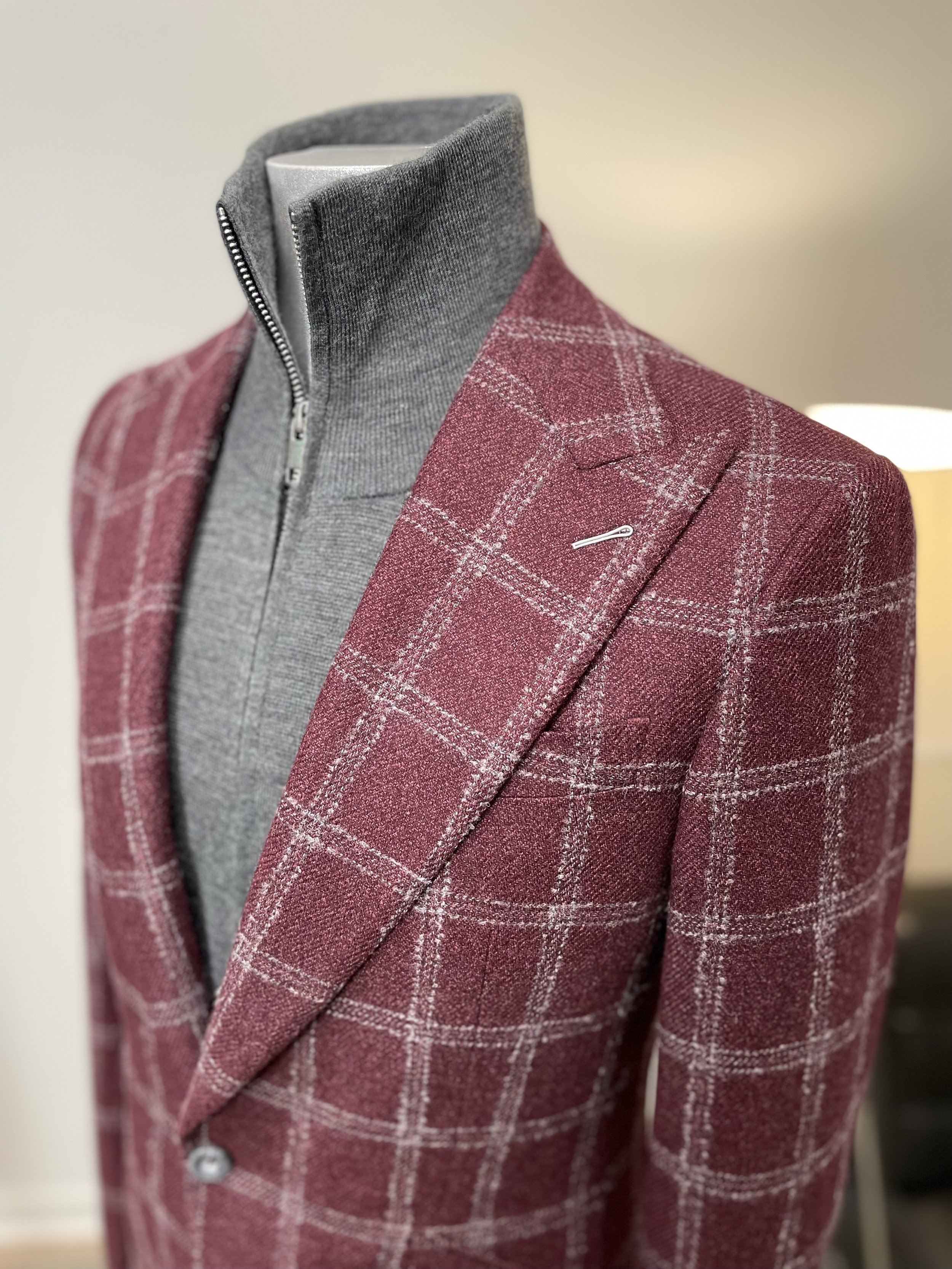 A mannequin dressed in a gray zip-up turtleneck and a red plaid blazer displayed indoors.