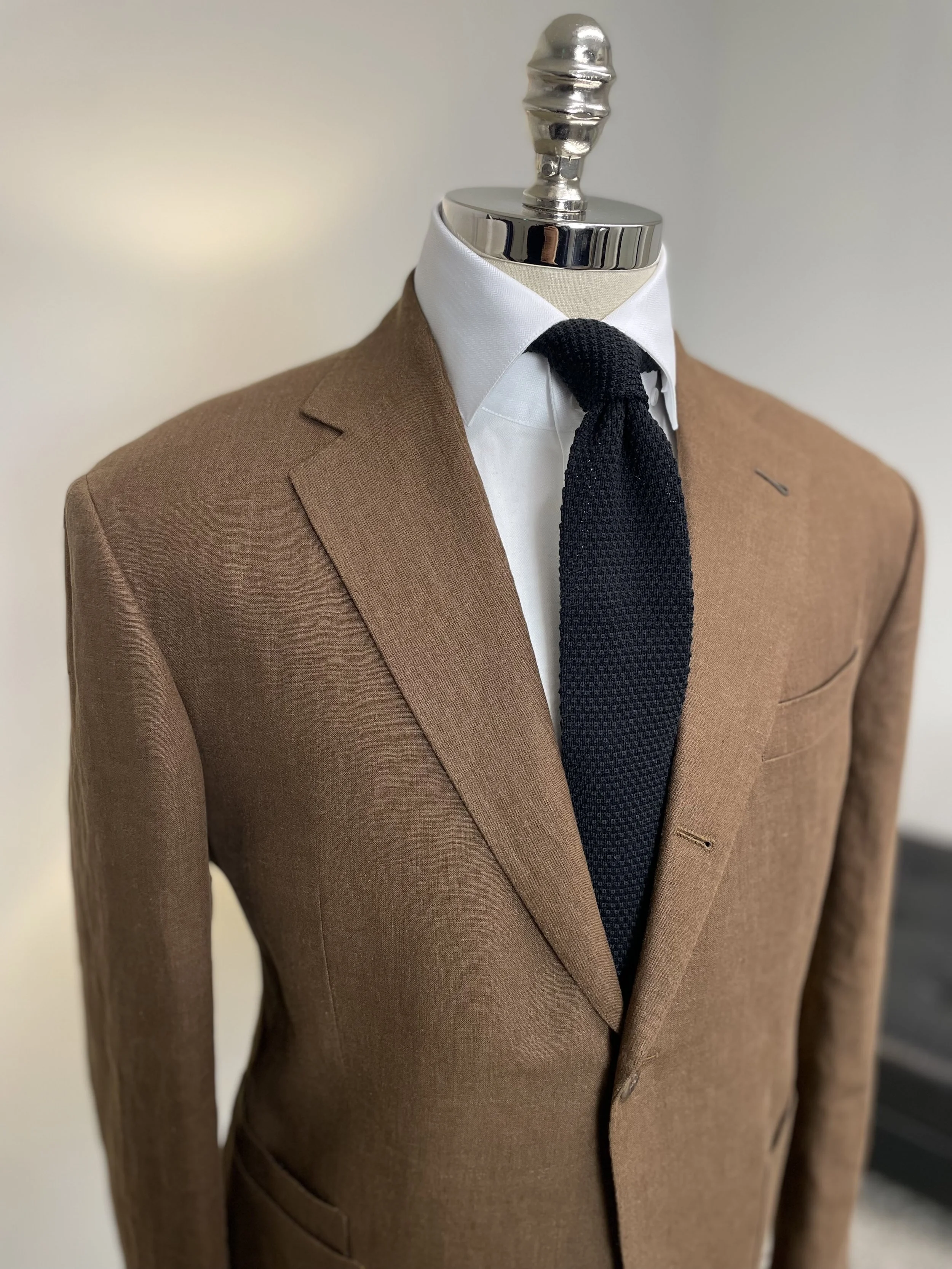 Close-up of a mannequin dressed in a brown suit jacket, white dress shirt, and black tie.