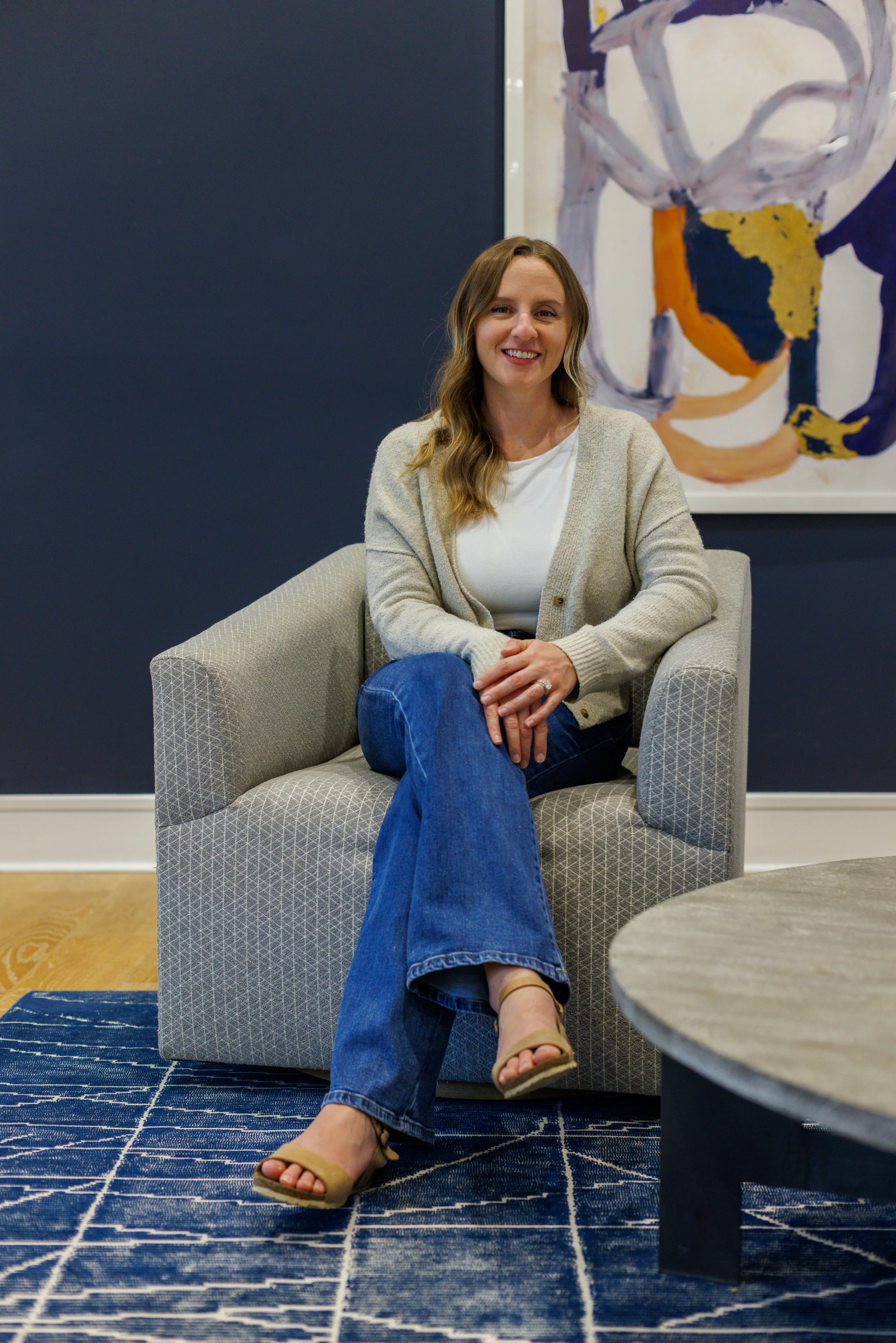 picture of woman with light brown hair sitting in a chair with legs crossed smiling at the camera