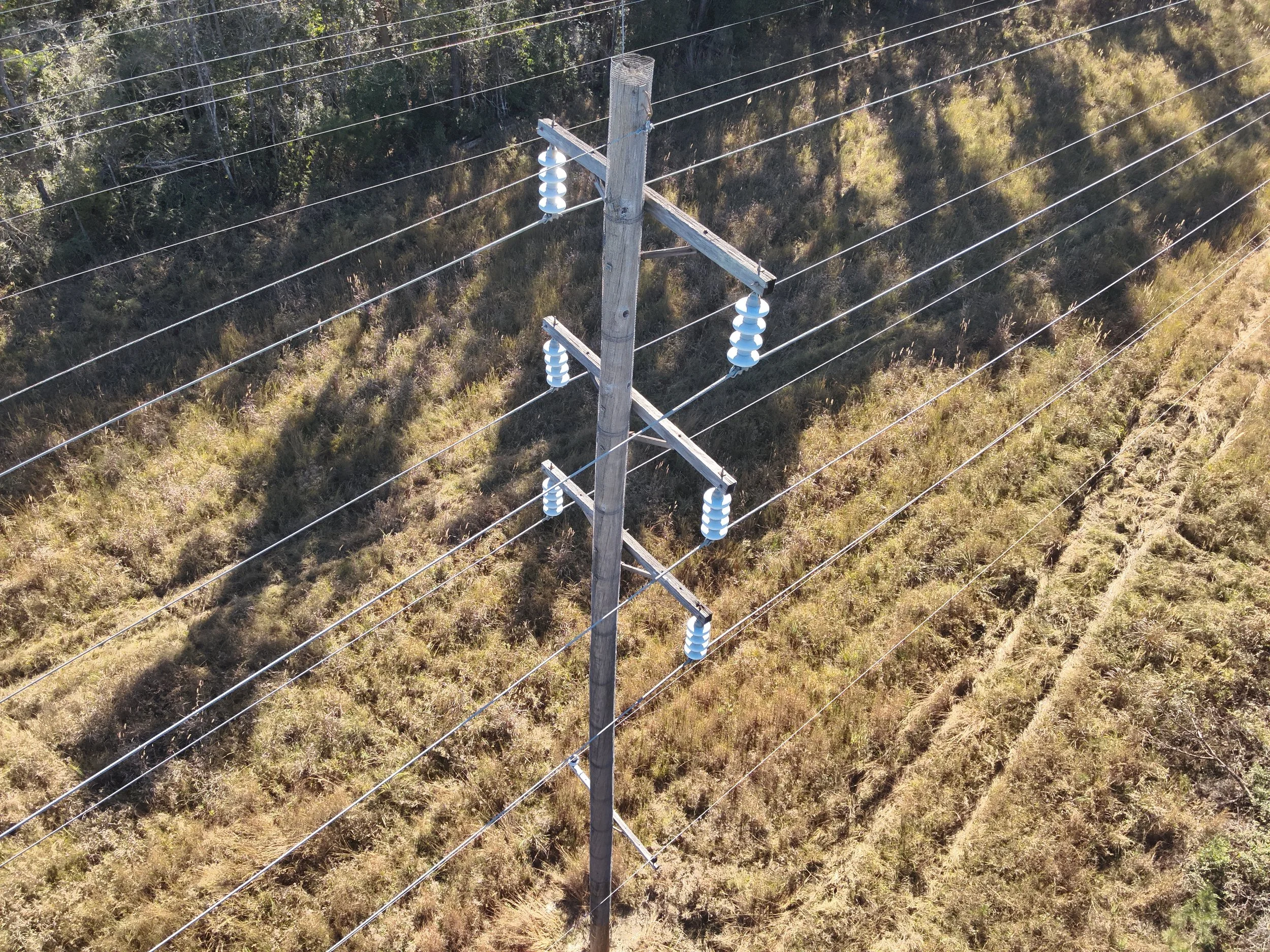 Aerial view of an electrical utility pole with insulators supporting multiple power lines in a grassy field.