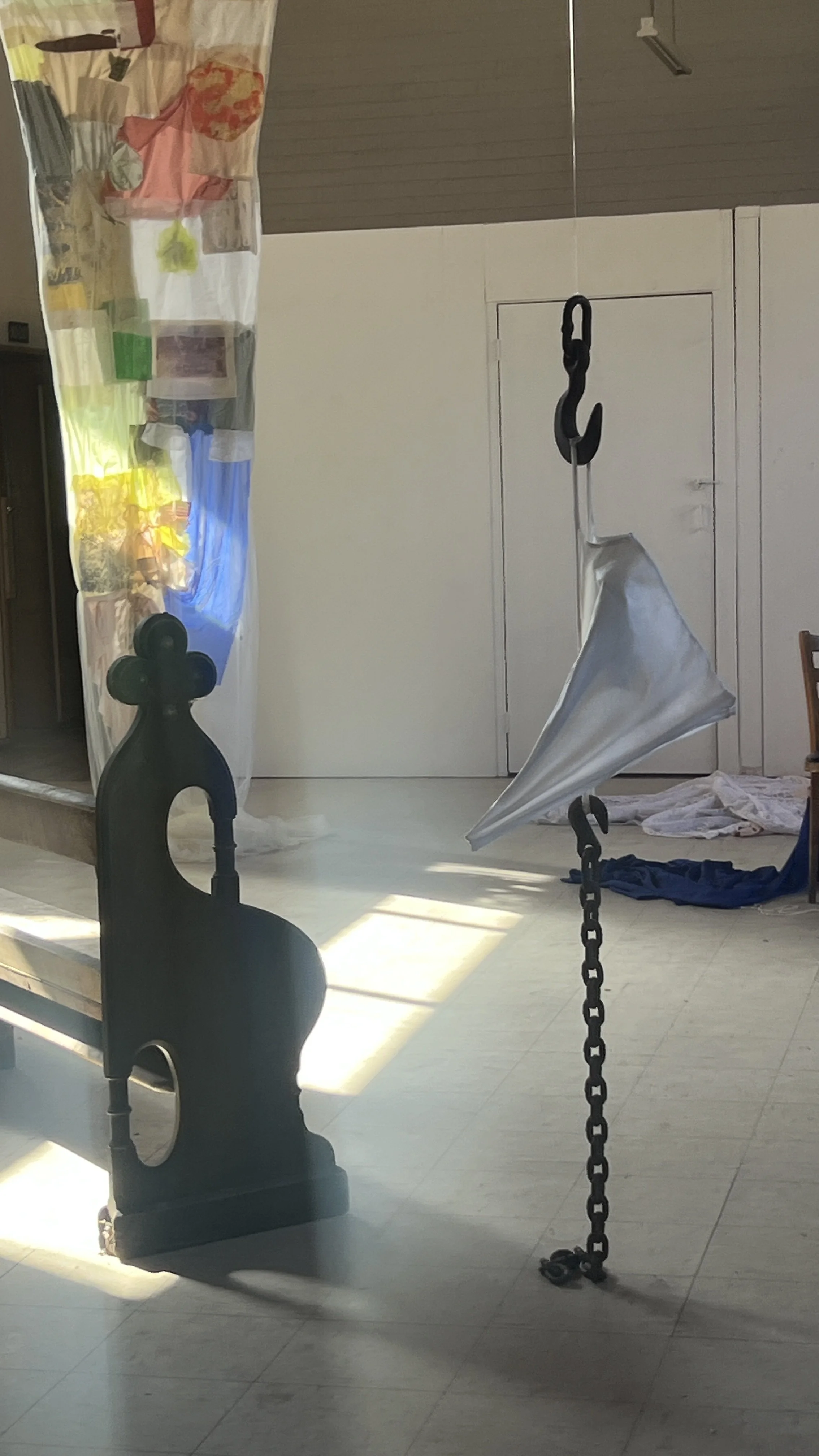 A hanging object made of a metal chain with an umbrella attached to it, in a room with sunlight and scattered clothes on the floor.