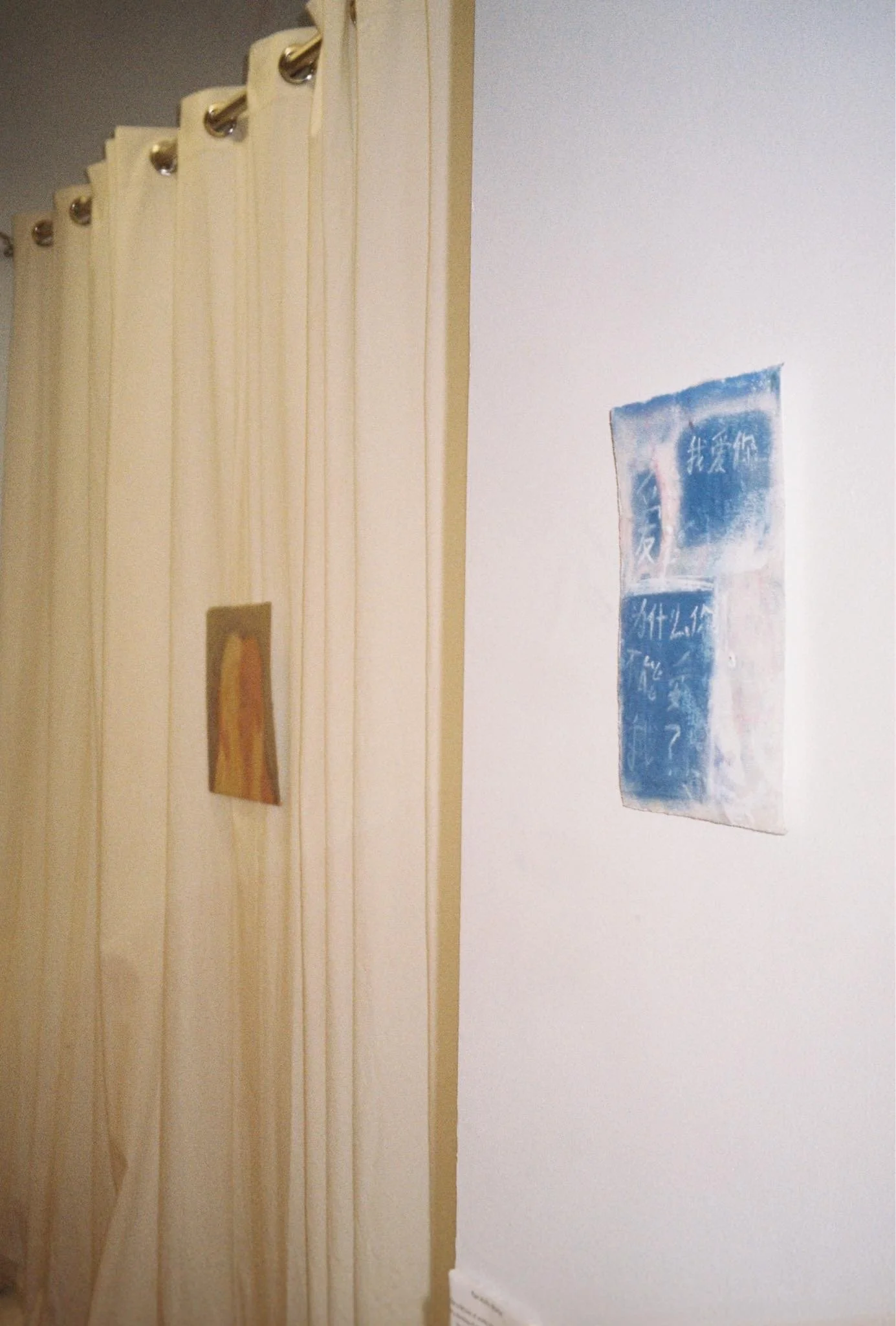 Part of an art gallery with two small paintings on white and beige walls.
