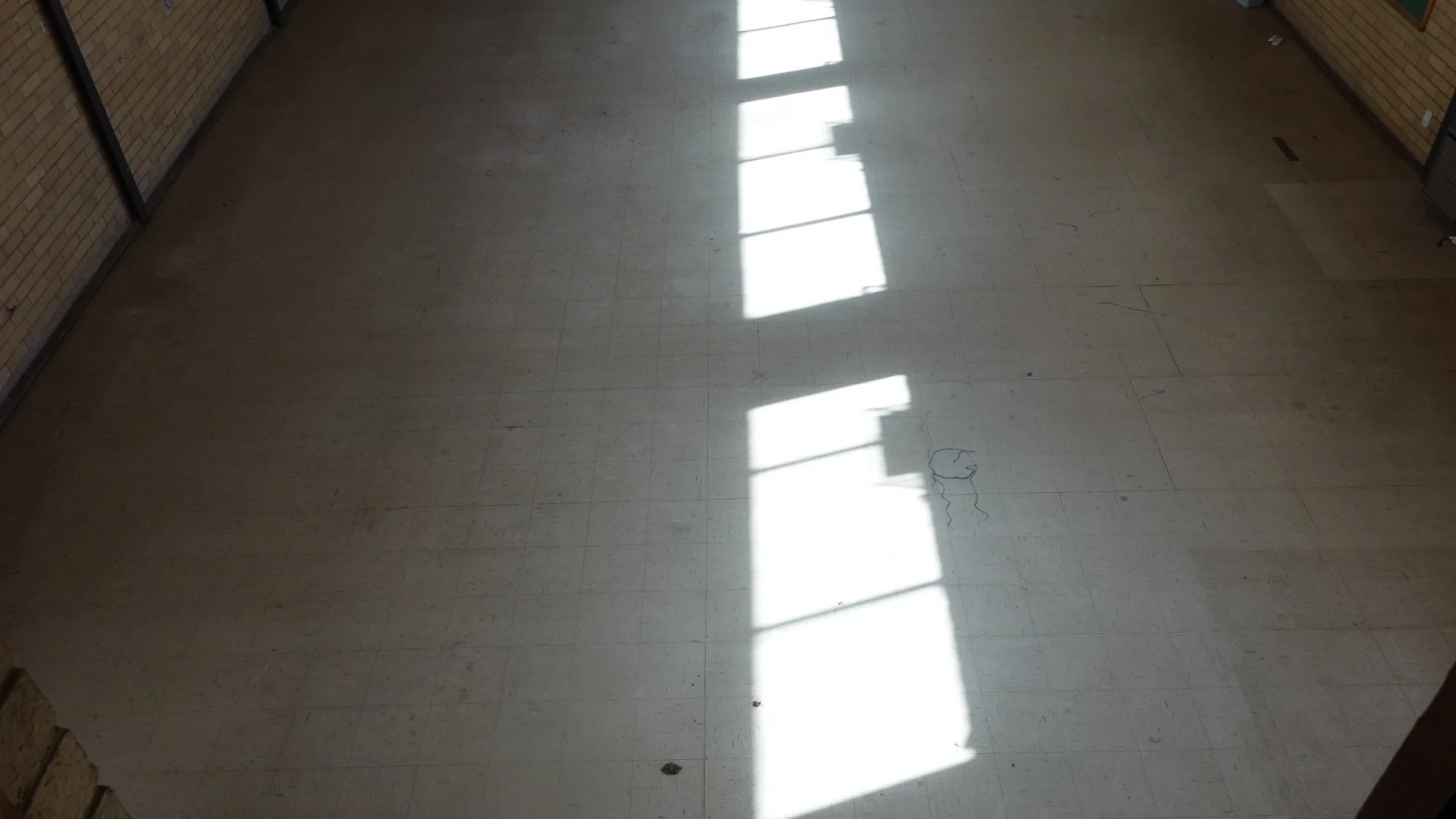 Empty tiled floor with sunlight and shadow from windows creating rectangular patterns.