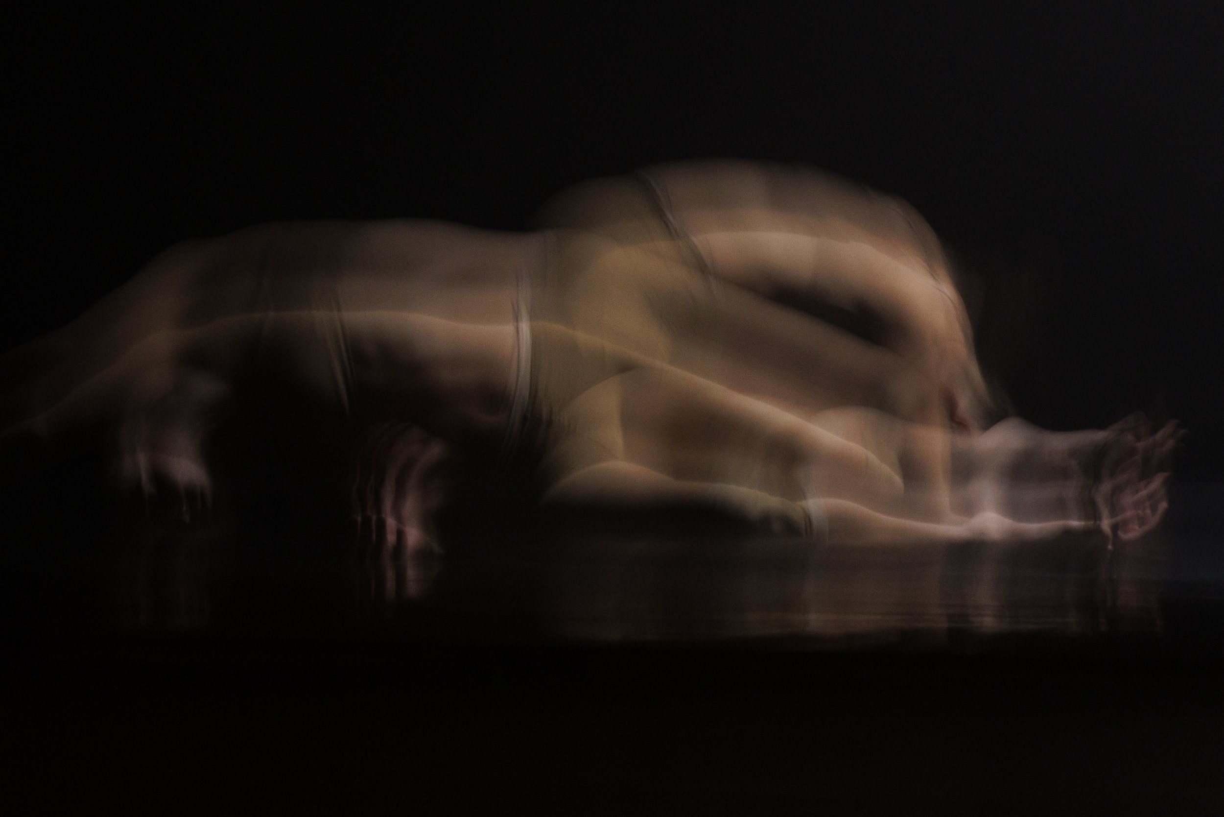 Blurred image of a person in a crawling position on a dark stage or studio floor