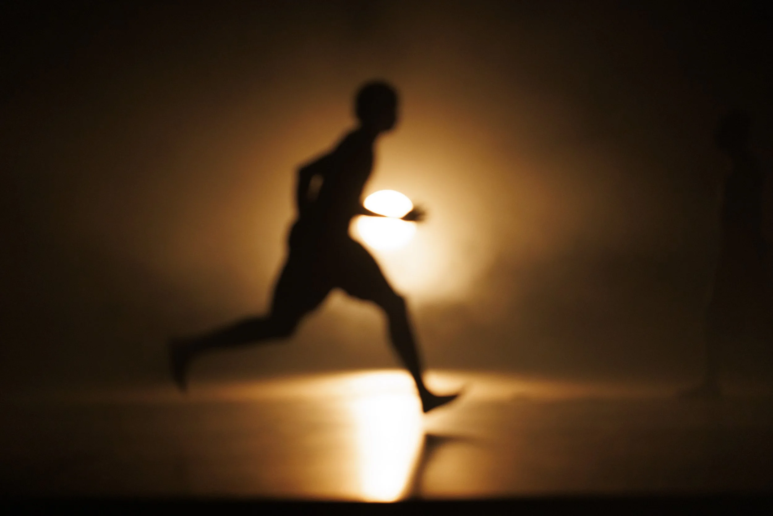 Silhouette of a person running during sunset or sunrise, with a bright sun in the background.