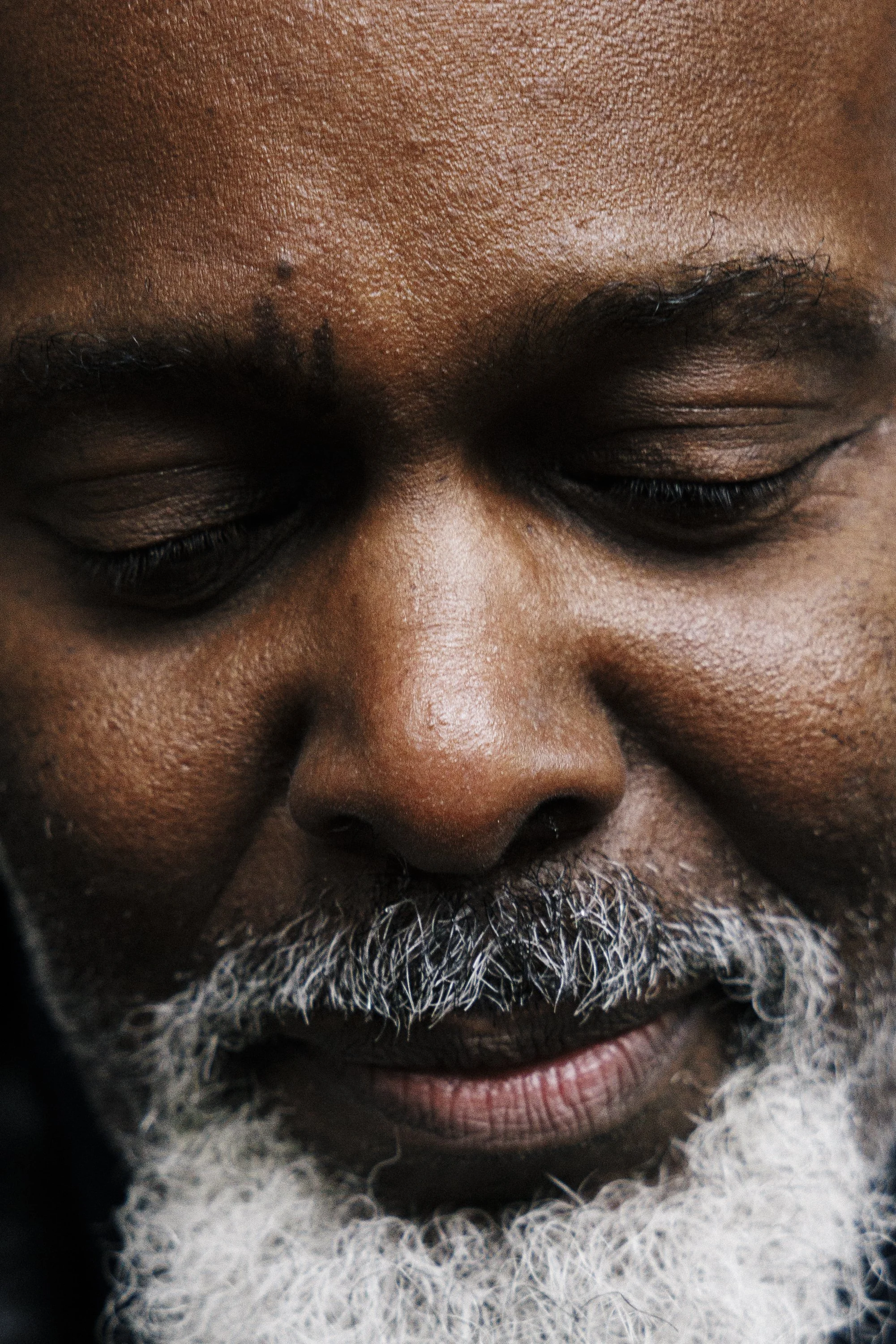 Close-up of a man's face with eyes closed, showing dark skin, a gray beard, and a mustache.