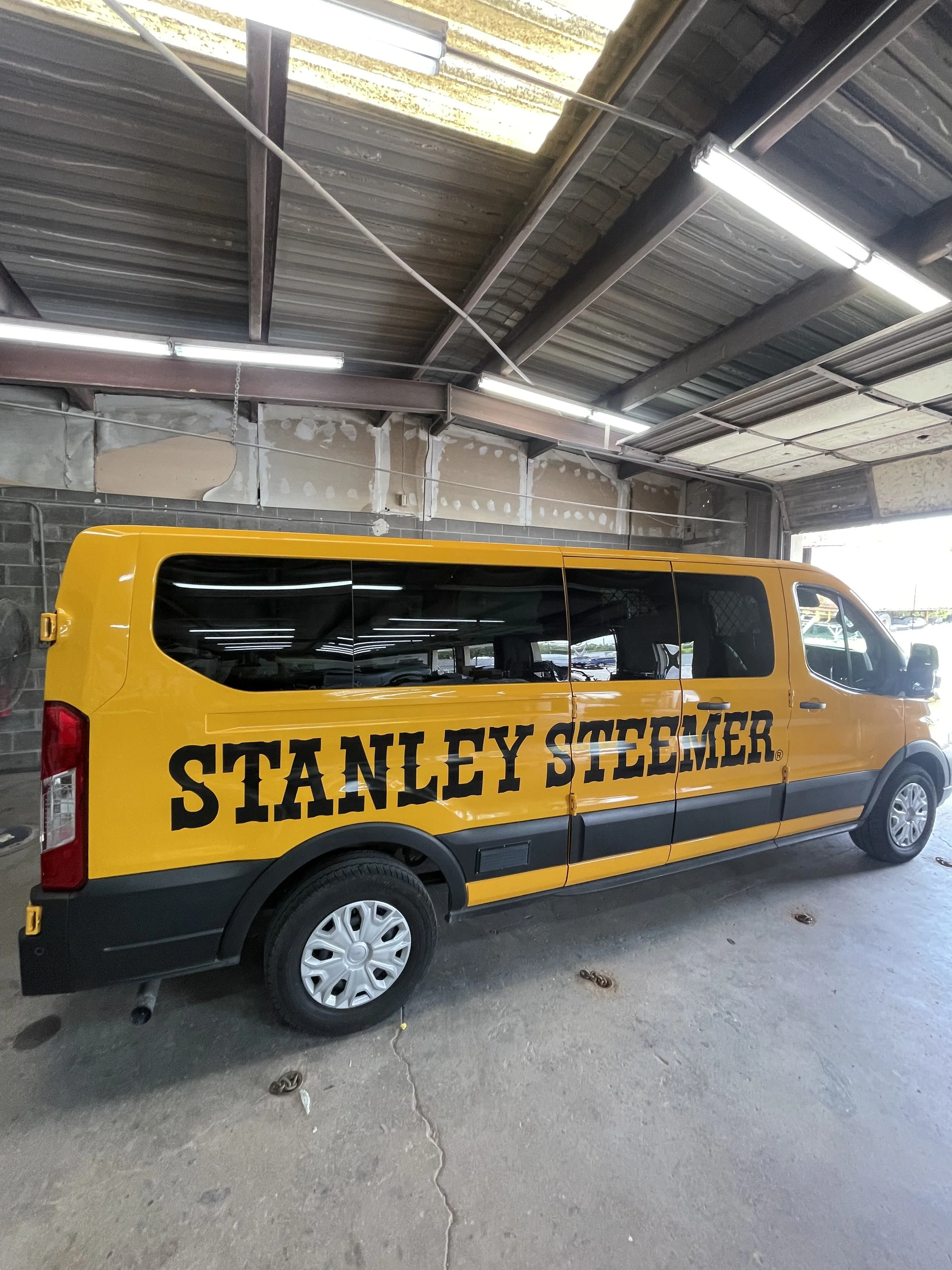 A yellow service van with black lettering reading 'STANLEY STEEMER' parked inside a garage or warehouse.
