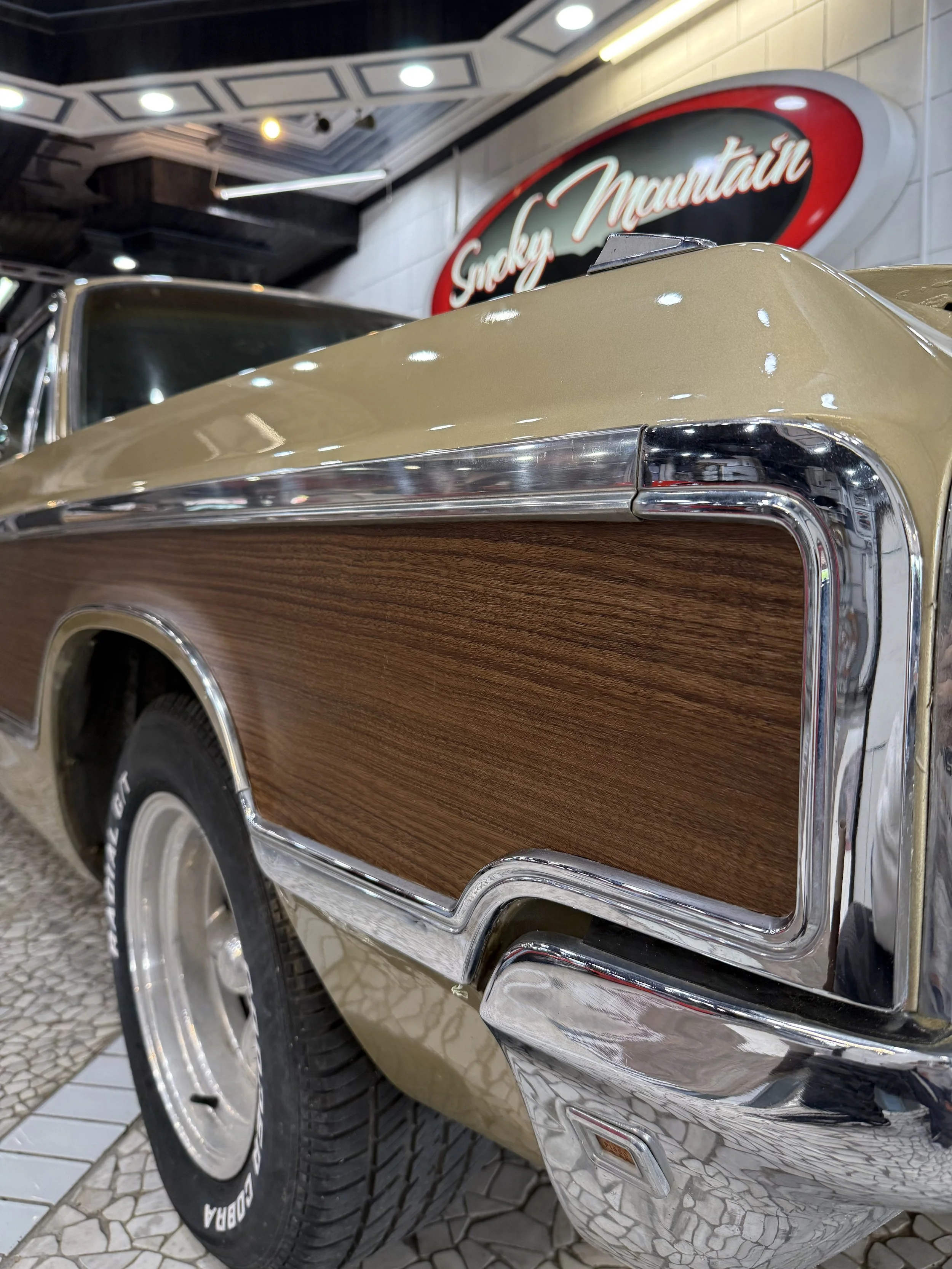 Close-up of a vintage car with beige paint, wood paneling on the side, and chrome accents, displayed indoors at a museum.