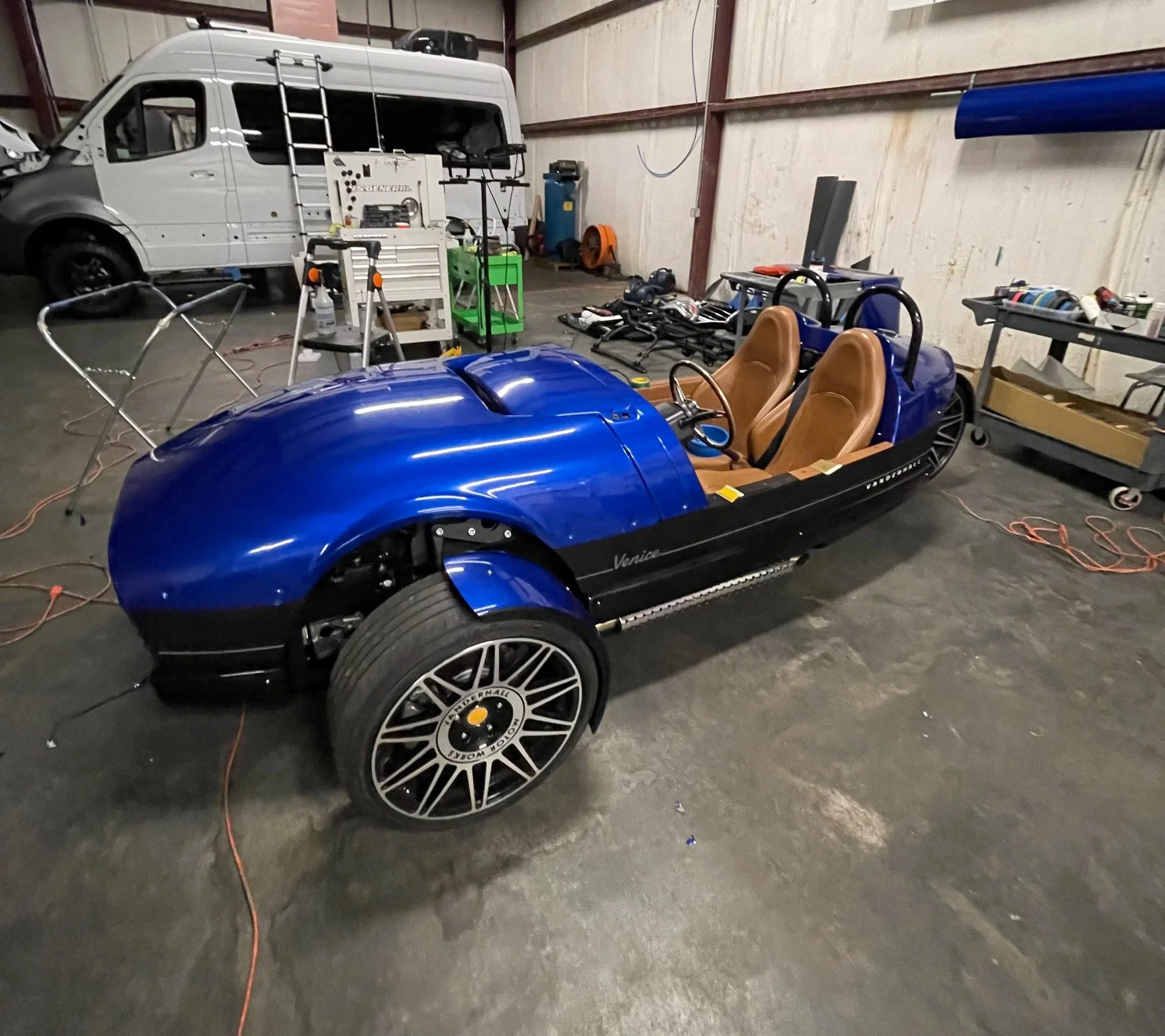 Blue racing go-kart with tan seats inside a workshop, surrounded by tools and equipment.