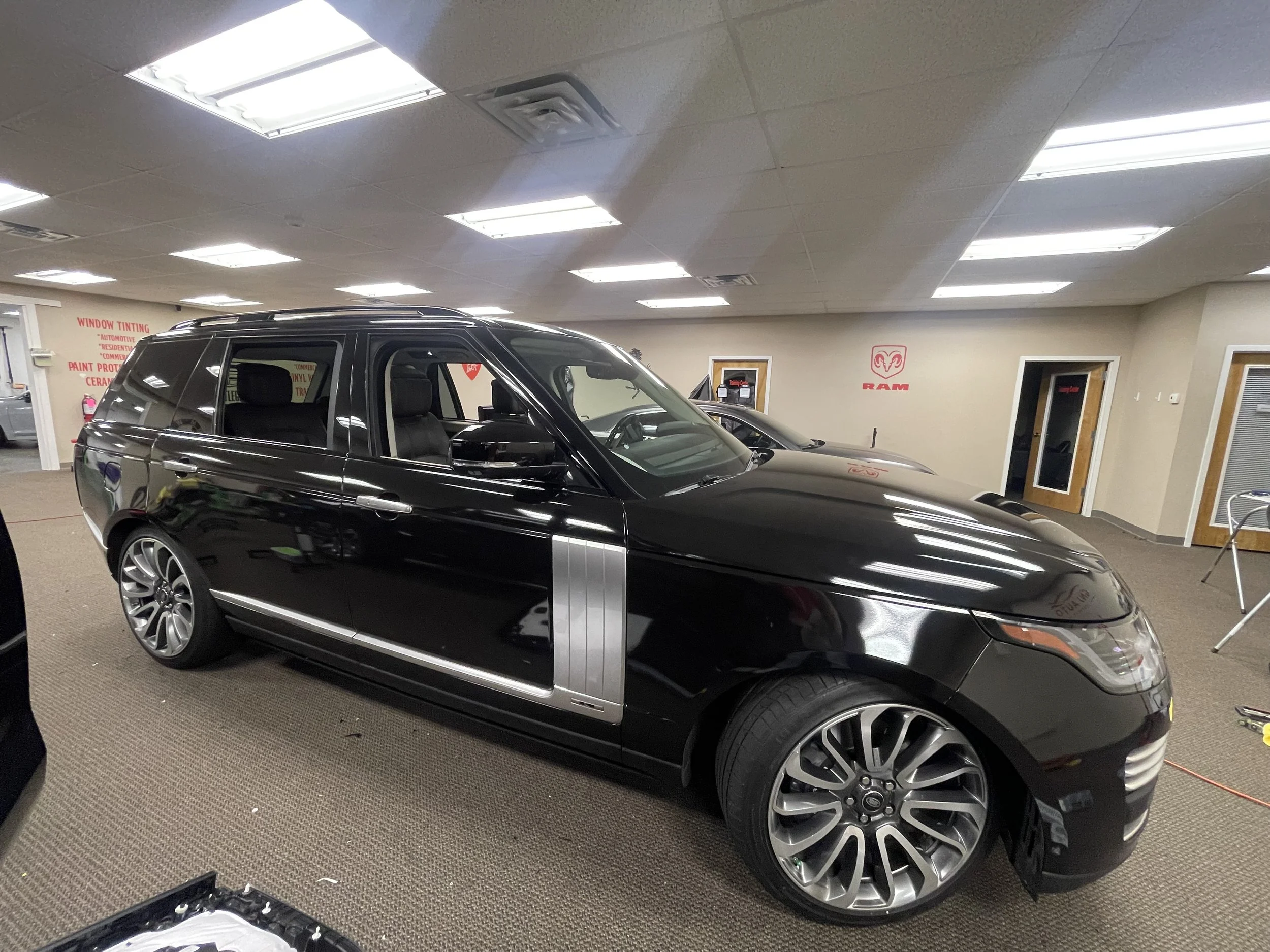 A black luxury station wagon with silver accents parked indoors in a showroom or service area, with ram logo and other vehicles visible in the background.