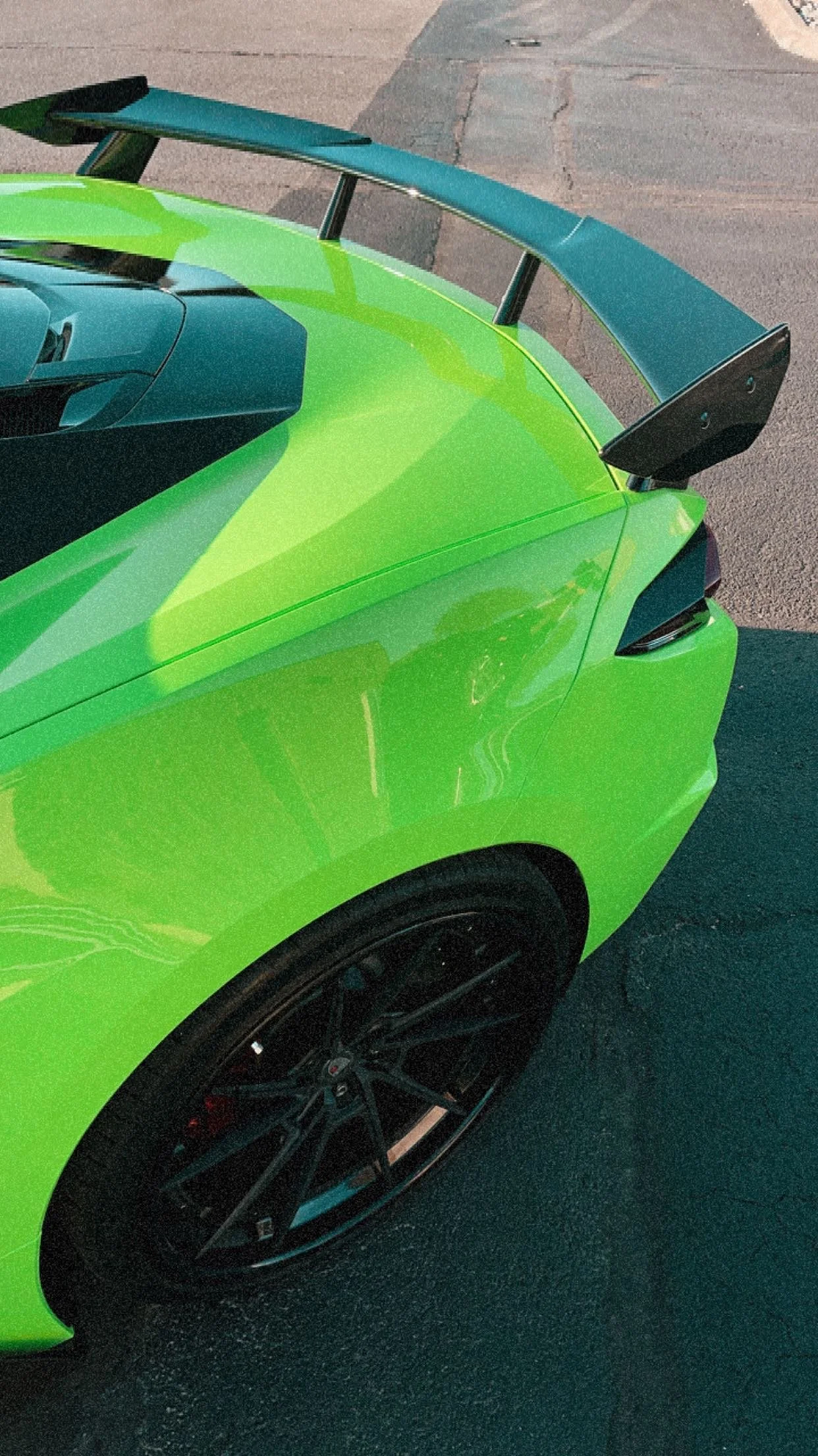 Close-up of a bright green sports car with a black rear wing, black wheels, and a sleek, aerodynamic design.
