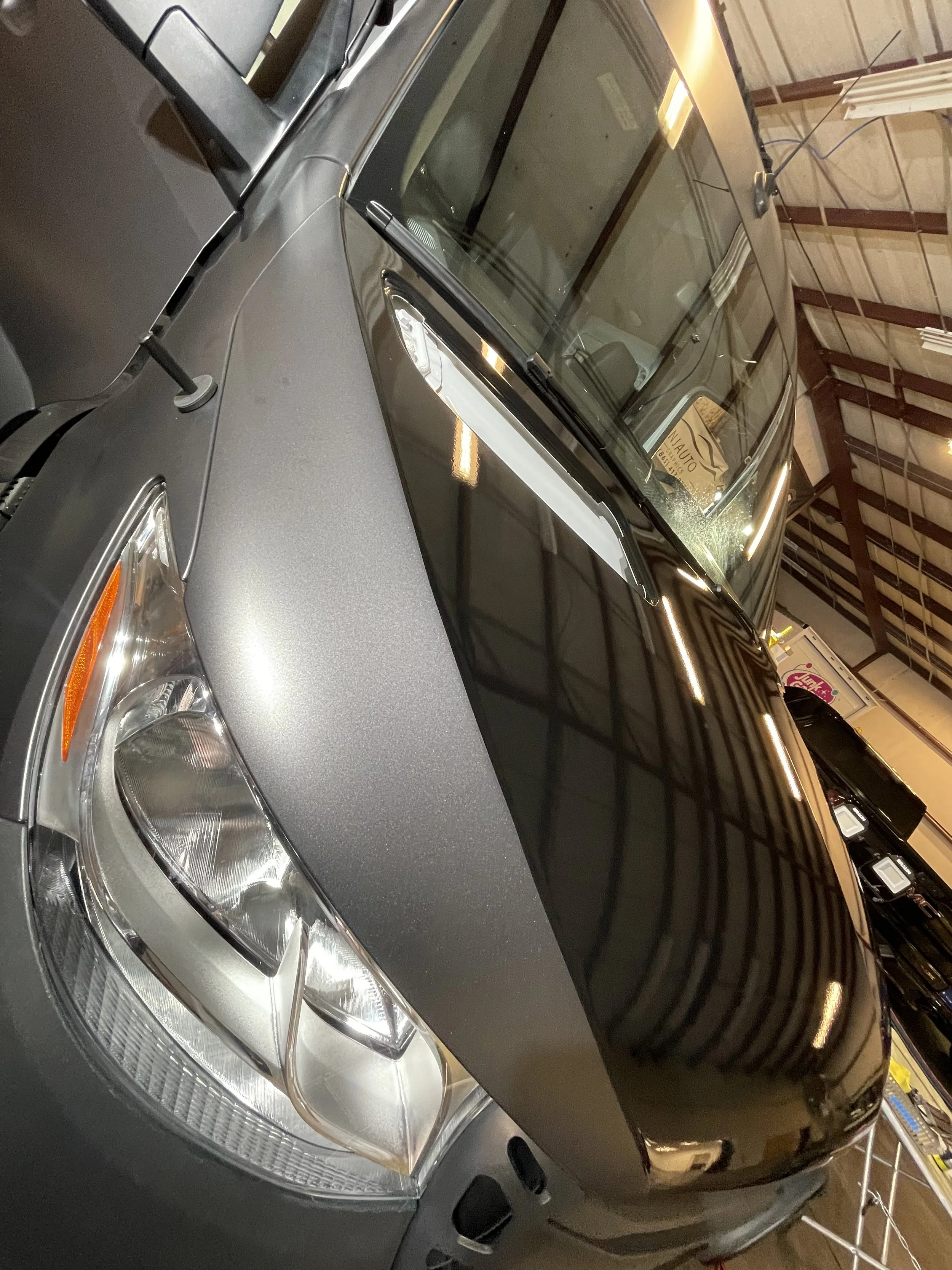 A dark gray or black Jeep SUV parked inside a warehouse or garage, with the front of the vehicle visible and the roof reflecting overhead lights.