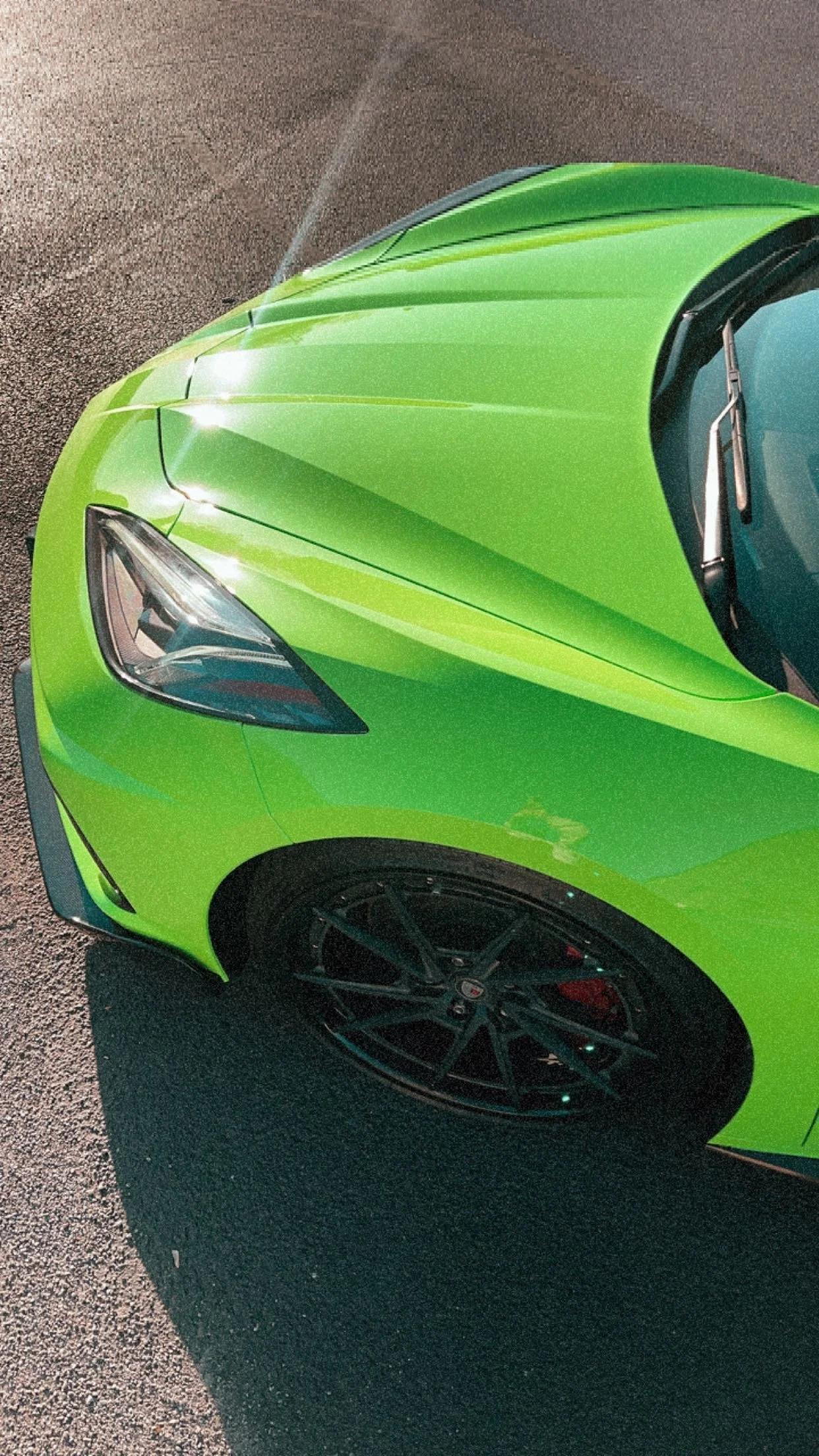 Close-up of the front part of a bright green sports car with black wheels and large headlights parked on asphalt.