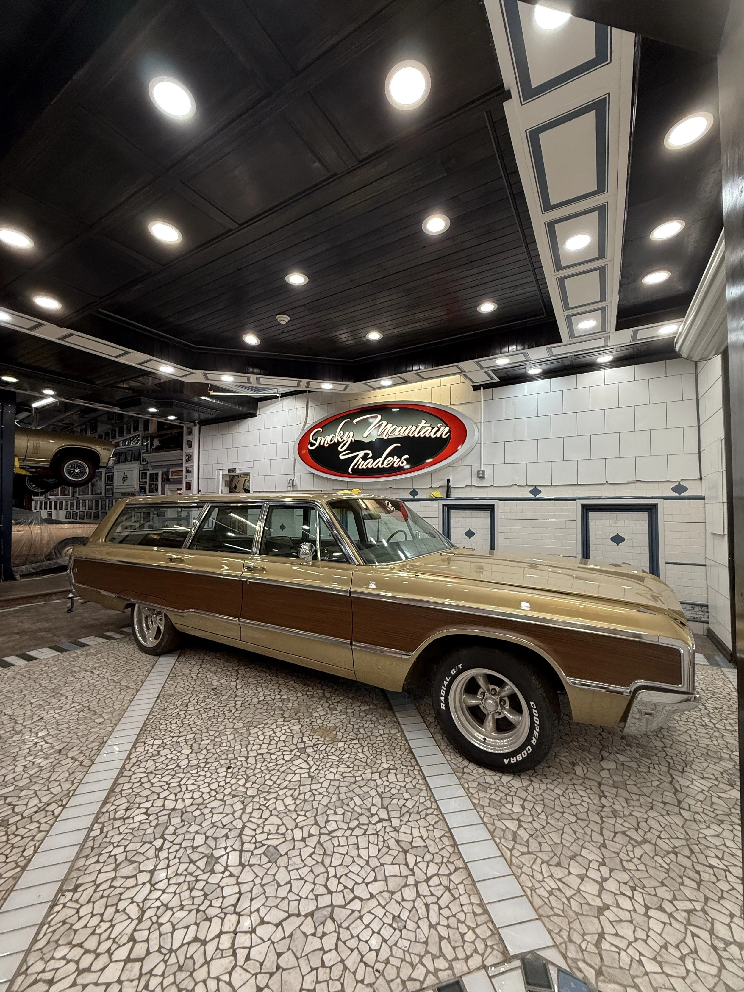 A vintage station wagon with a wood panel exterior on display inside a showroom, with a sign that reads "Smoky Mountain Traders" in the background.