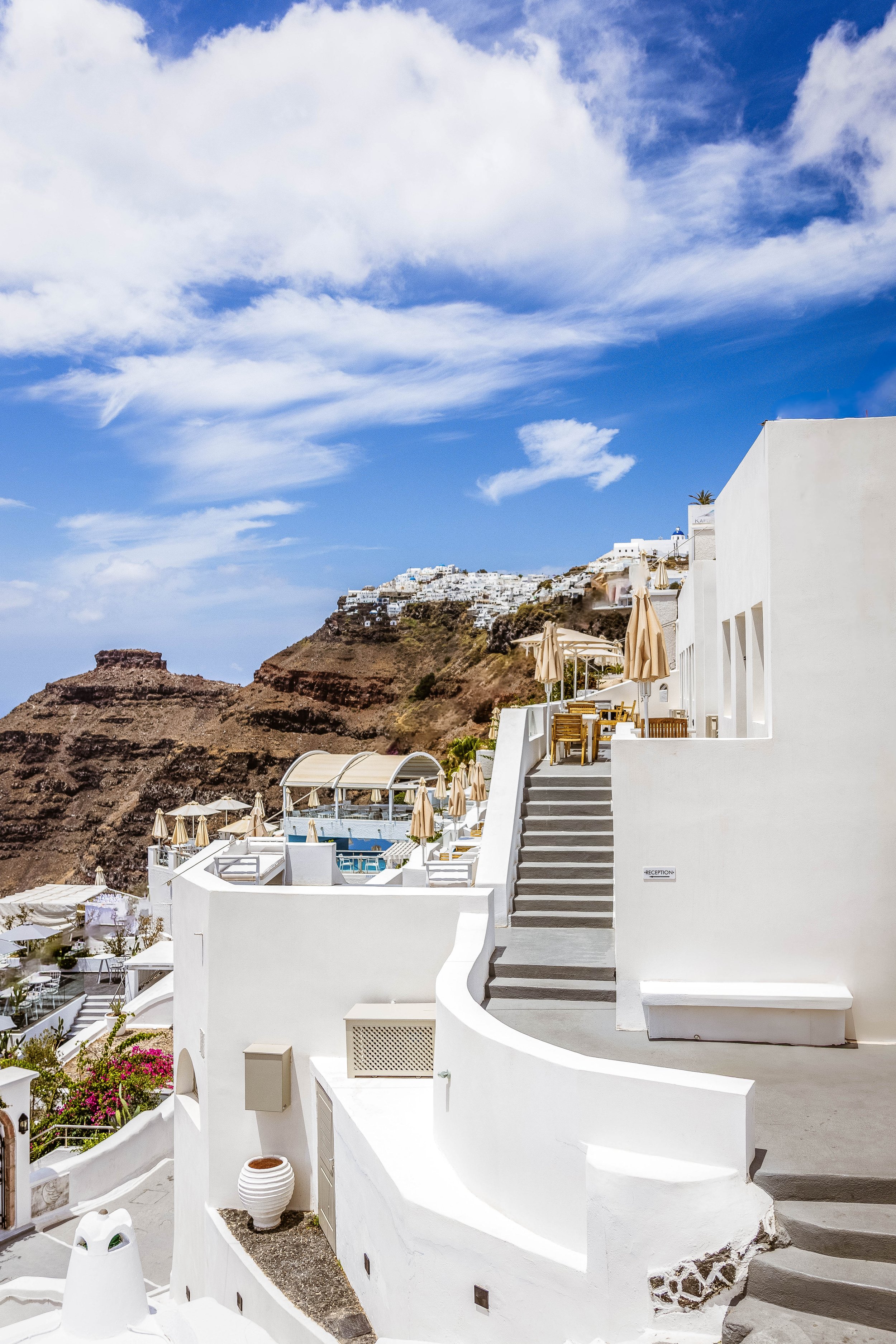 I remember the hush — just after noon — when the light softened into silk and the stairs shimmered like a quiet invitation.
This frame carries the poise of Cycladic hospitality — curved walls, sun-washed textures, and the rhythm of rest unfolding on