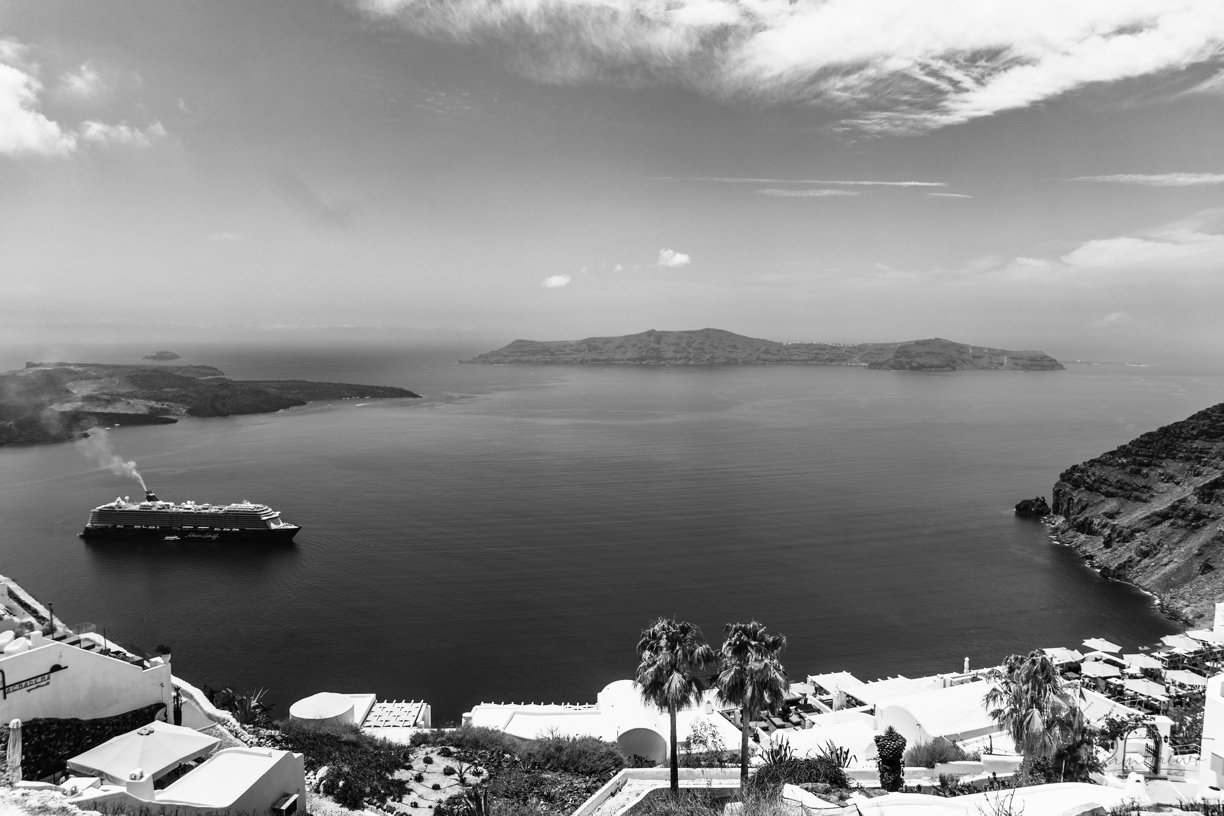 Some frames don’t need color to breathe.
This was one of them.
I stood in silence as the caldera stretched out like a forgotten page — black, silver, and endless. The cruise ship cut gently across the sea like a thought in transit, while Santorini s
