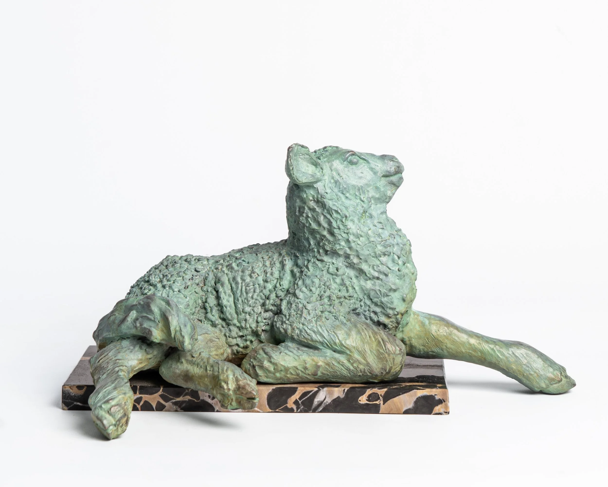 Bronze sculpture of a reclining dog with a sheep's head, lying on a patterned stone base.