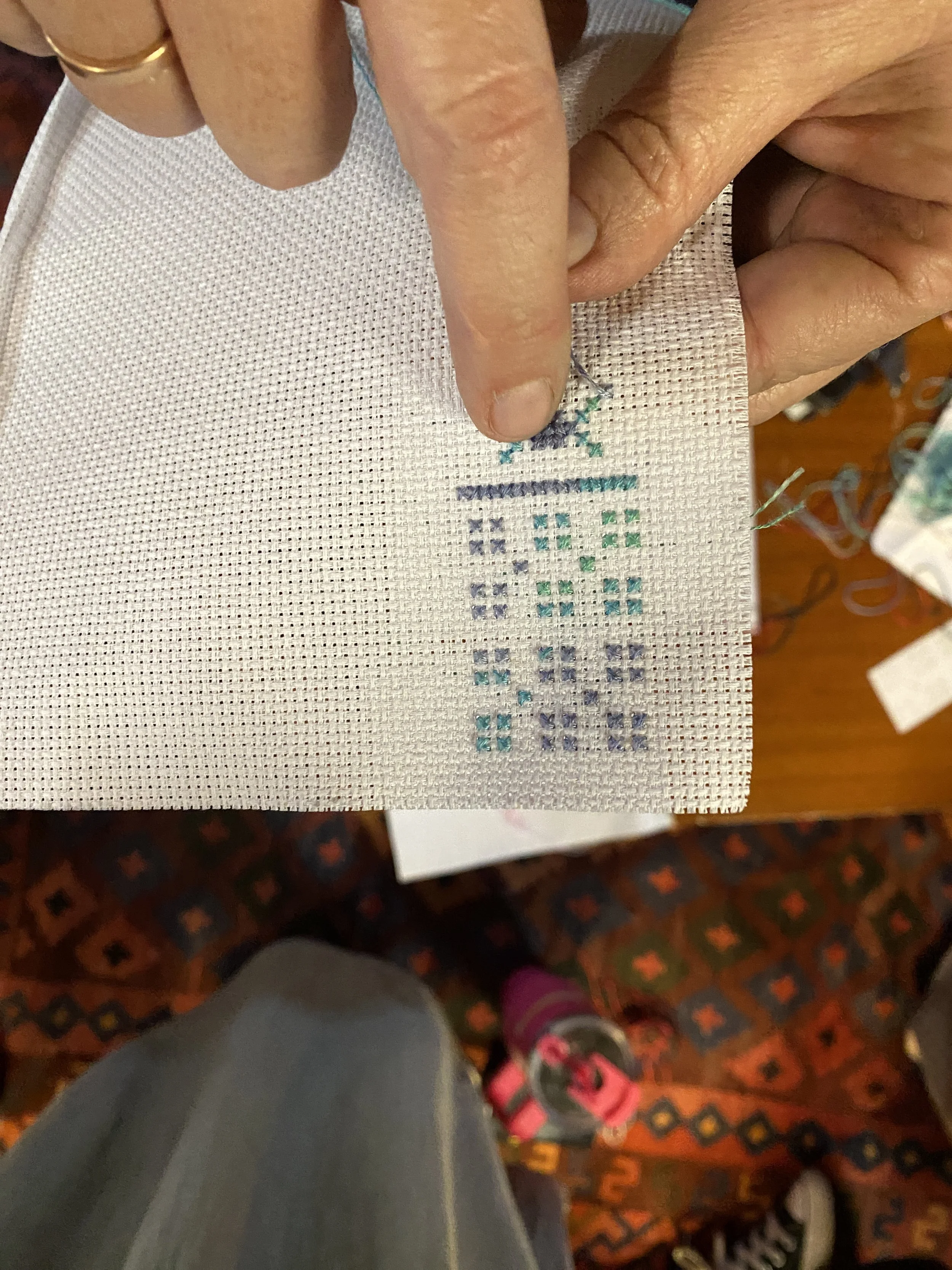 Close-up of a person's hand holding aida cloth with cross-stitch pattern being worked on.