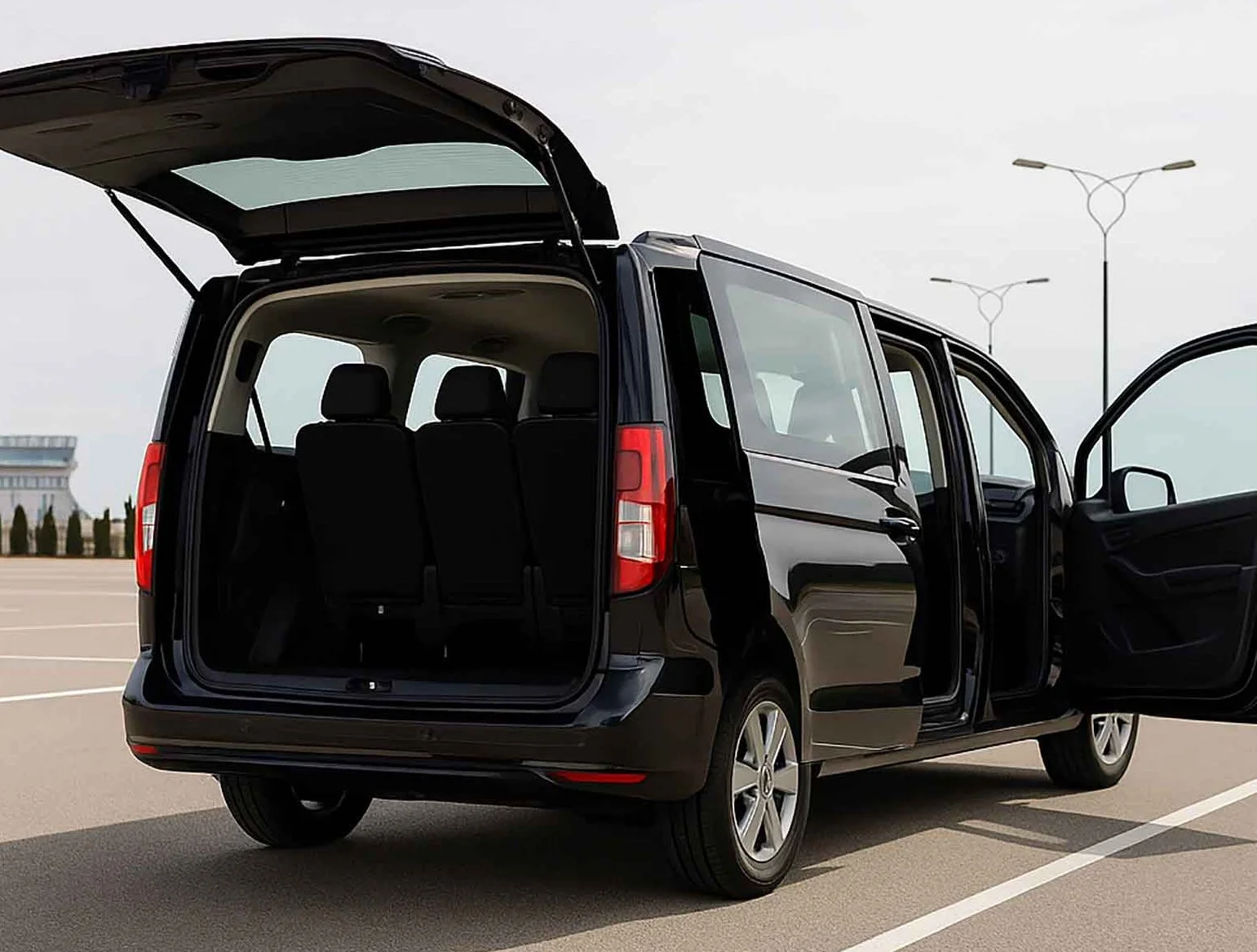 Black minivan with open rear hatch and front door open, parked in an empty parking lot.
