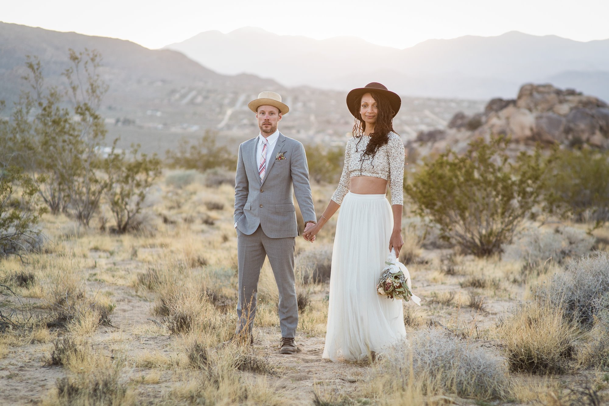 Bride in hat and groom in suit pose stylishly in the Joshua Tree desert