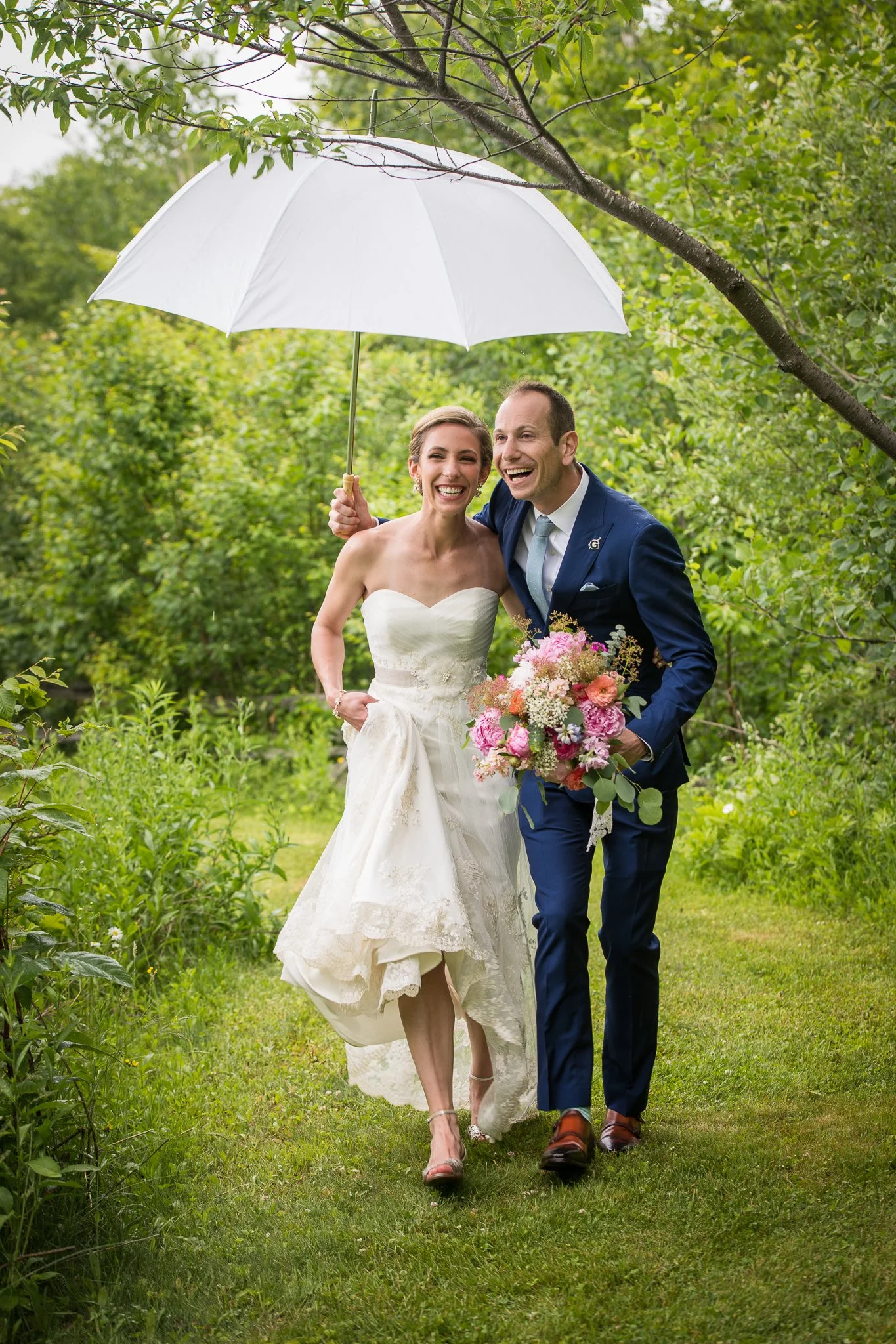 Bride and groom walking and laughing together under an umbrella at The Ponds at Bolton Valley in Bolton, Vermont. A natural, unposed wedding portrait moment