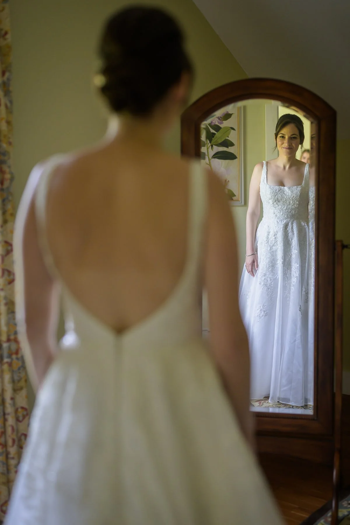 Chelsea stands in her wedding dress at the Inn at Manchester in Vermont, seen reflected in a mirror during the getting-ready portion of the day. The portrait captures a quiet bridal moment before the ceremony.
