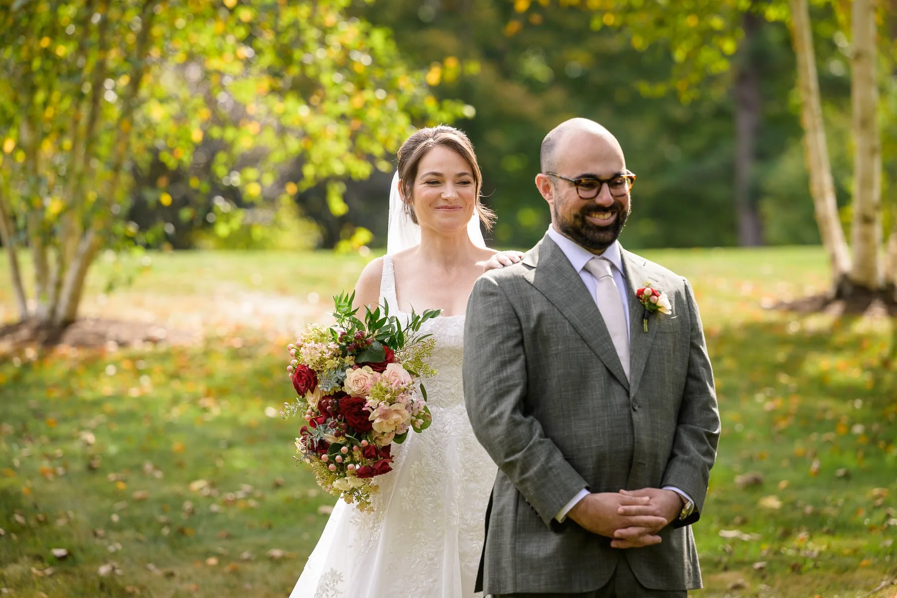 Chelsea places her hand on David’s shoulder during their first look at the Inn at Manchester in Vermont. Standing on the lawn with her bouquet in hand, she smiles as he waits to turn around.