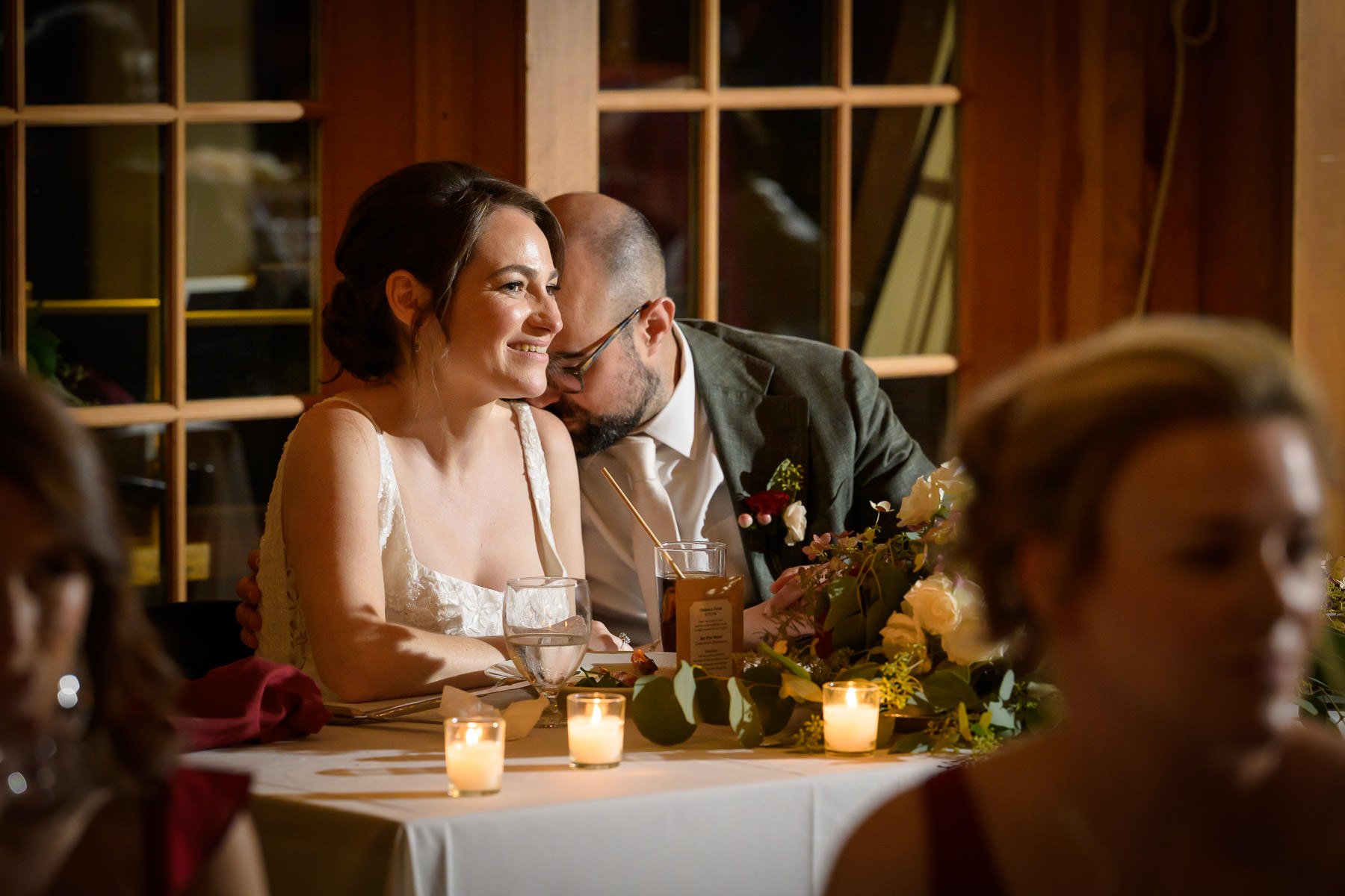 Chelsea and David sit together at their sweetheart table during the reception at the Inn at Manchester in Vermont. Surrounded by candlelight and florals, they share a quiet moment while taking in the celebration around them.