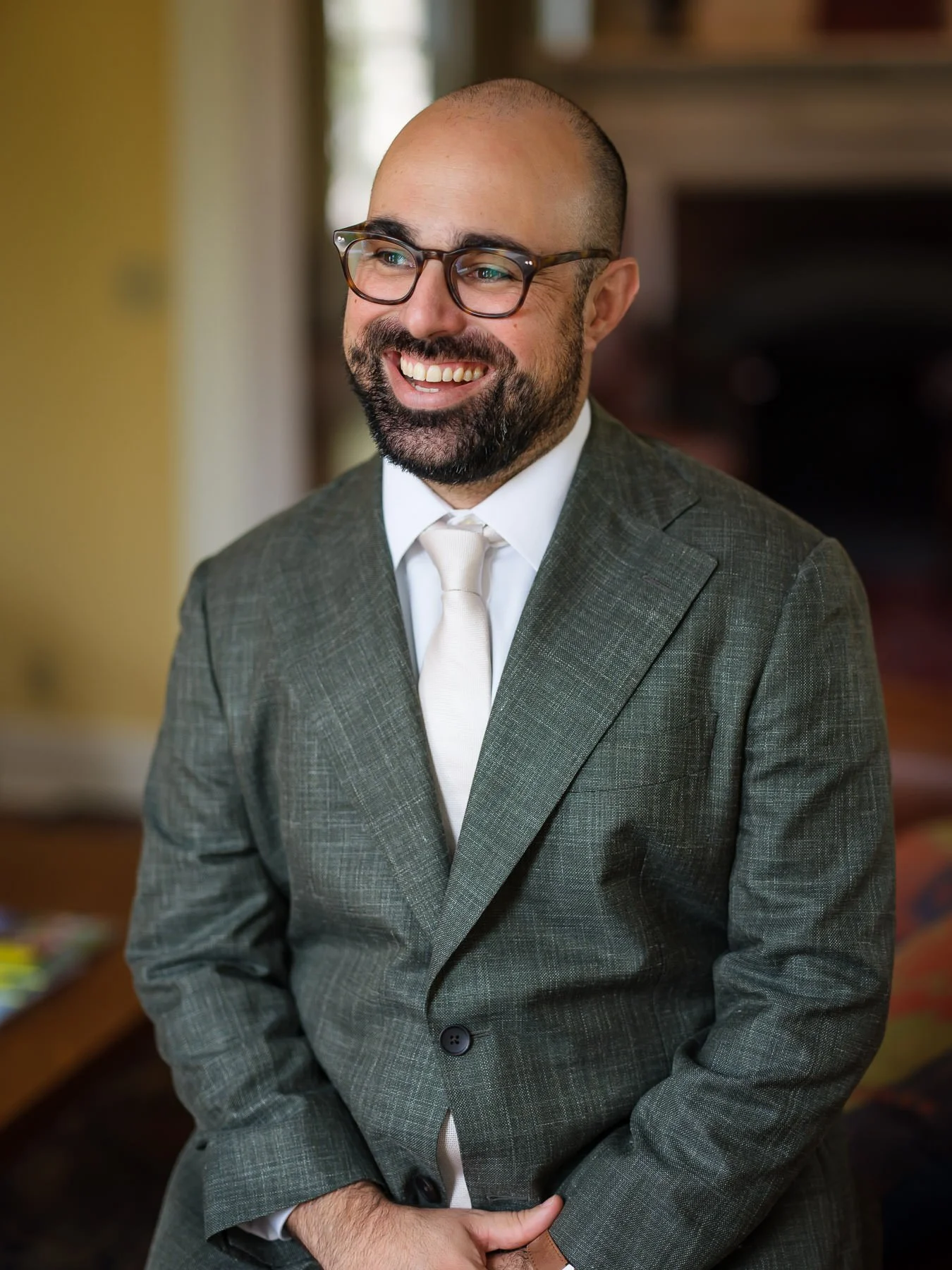 David smiles in a getting-ready portrait at the Inn at Manchester in Vermont, wearing a suit and light tie indoors before the ceremony. The image captures a relaxed moment as the wedding day begins.