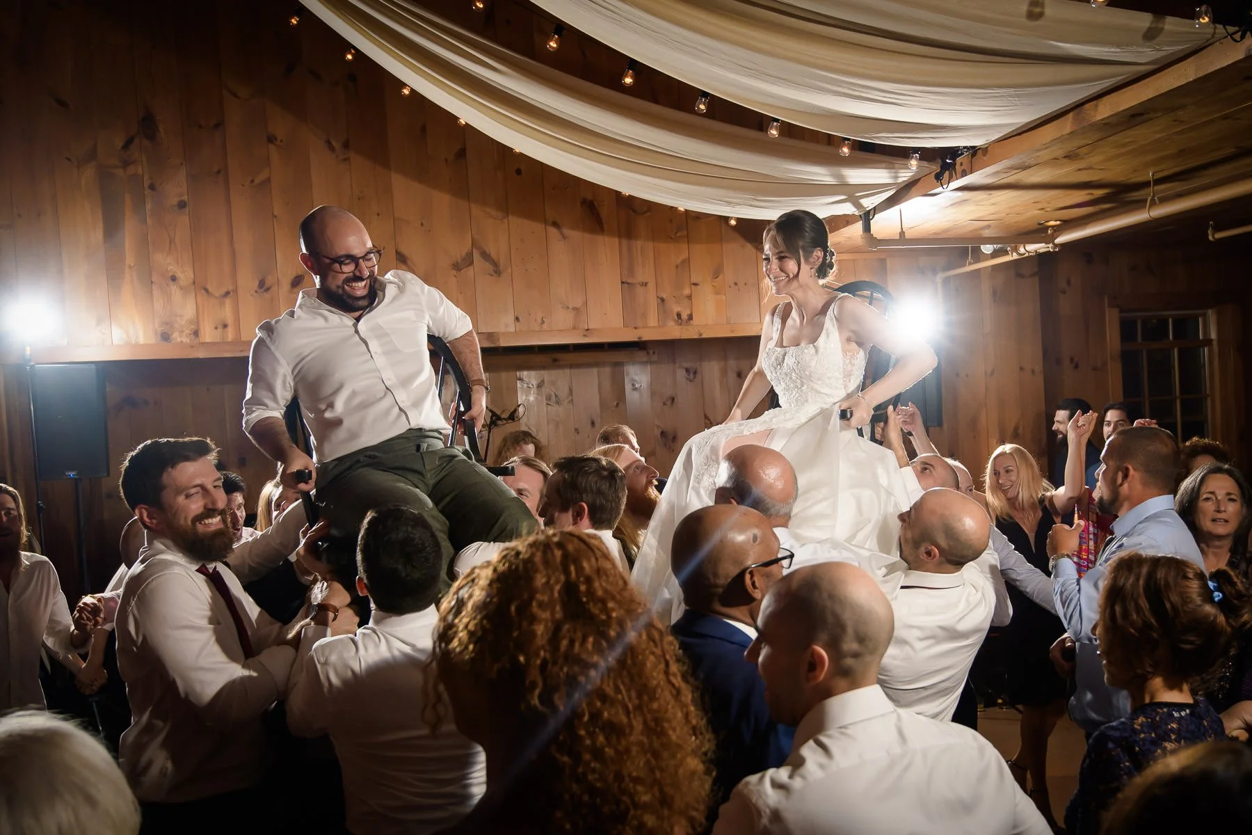 Chelsea and David are lifted on chairs during the hora at their reception at the Inn at Manchester in Vermont. Surrounded by cheering guests on the dance floor, the moment captures the energy and joy of the celebration.