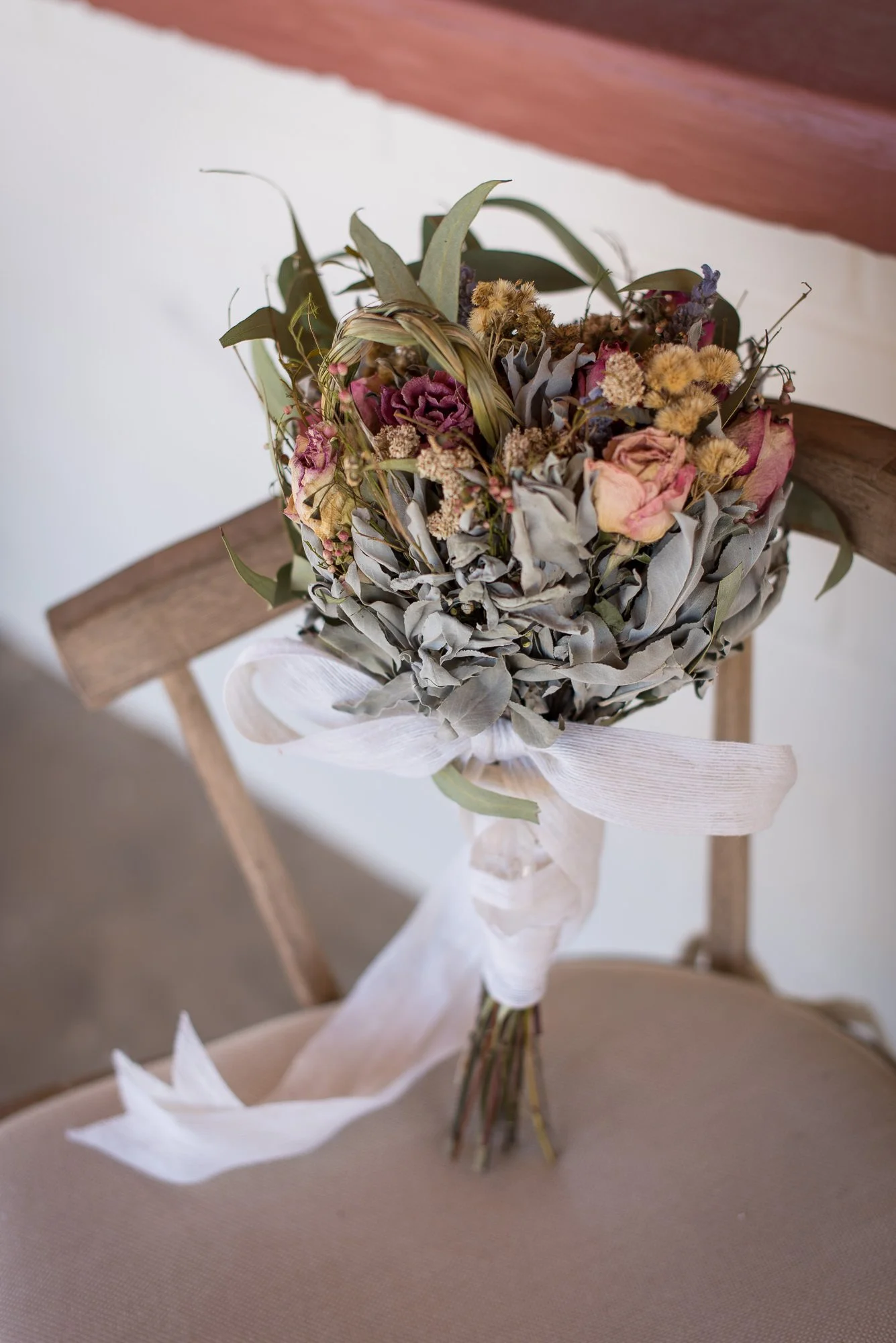 Boho-inspired wedding bouquet resting on a wooden chair in the desert light