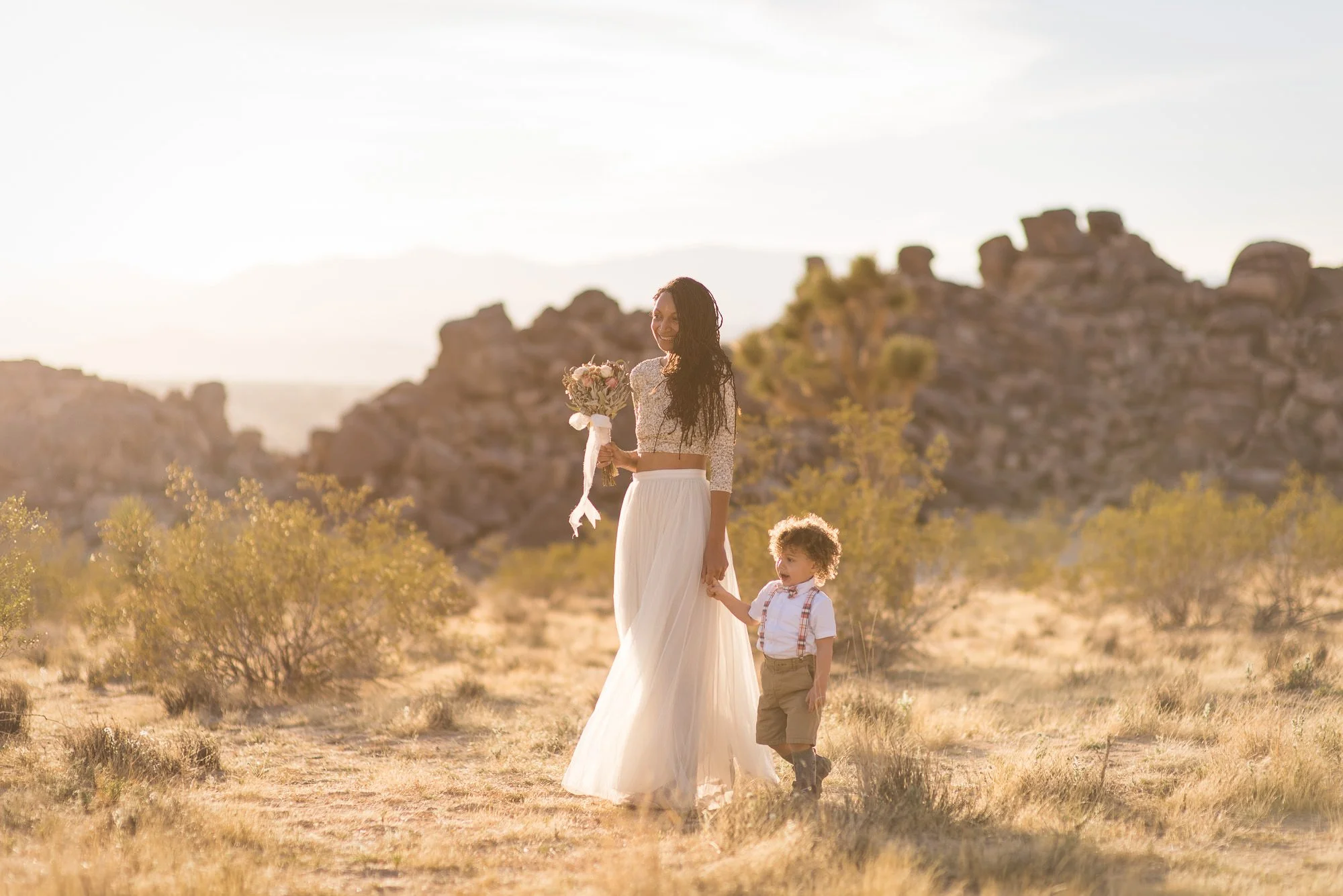 Bride walking through desert terrain with son before intimate Joshua Tree wedding